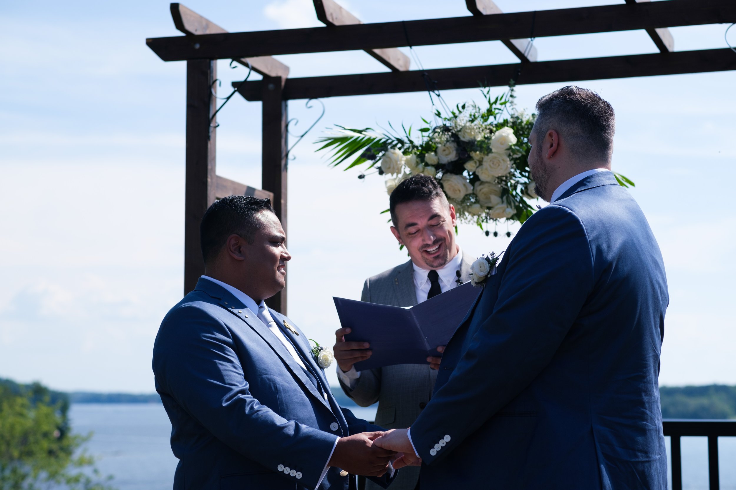  A color candid wedding photograph of Bryan + Adam exchanging wedding vows while their friend officiates  during their  outdoor wedding cermony  at the JW Marriot The Rosseau in Muskoka by Toronto wedding photographer Scott Williams  