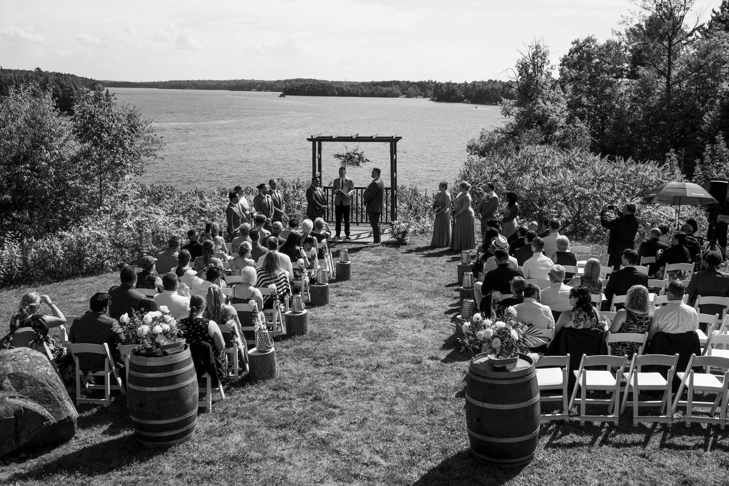  A black and white candid wedding photograph of Bryan + Adam  aisle during their  outdoor wedding ceremony overlooking the lake at the JW Marriot The Rosseau in Muskoka by Toronto wedding photographer Scott Williams  