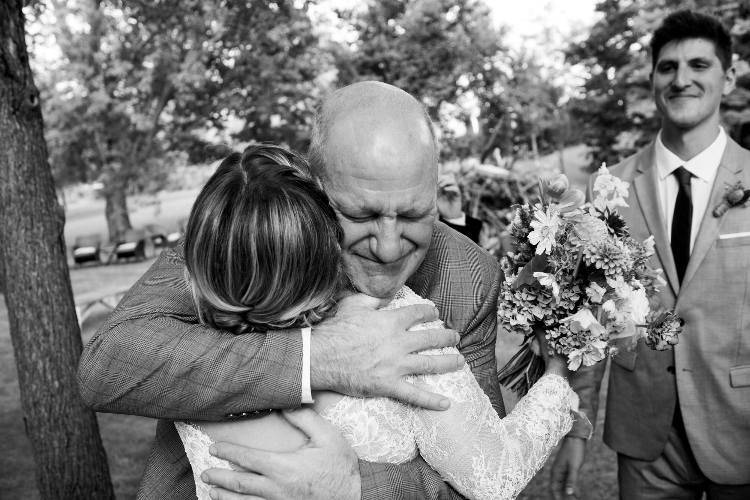  A black and white candid wedding photograph of the bride getting a hug from her new father in law after the ceremony at  her outdoor farm wedding near Pickering, Ontario by Toronto wedding photographer Scott Williams (www.scottwiliiamsphotographer.c