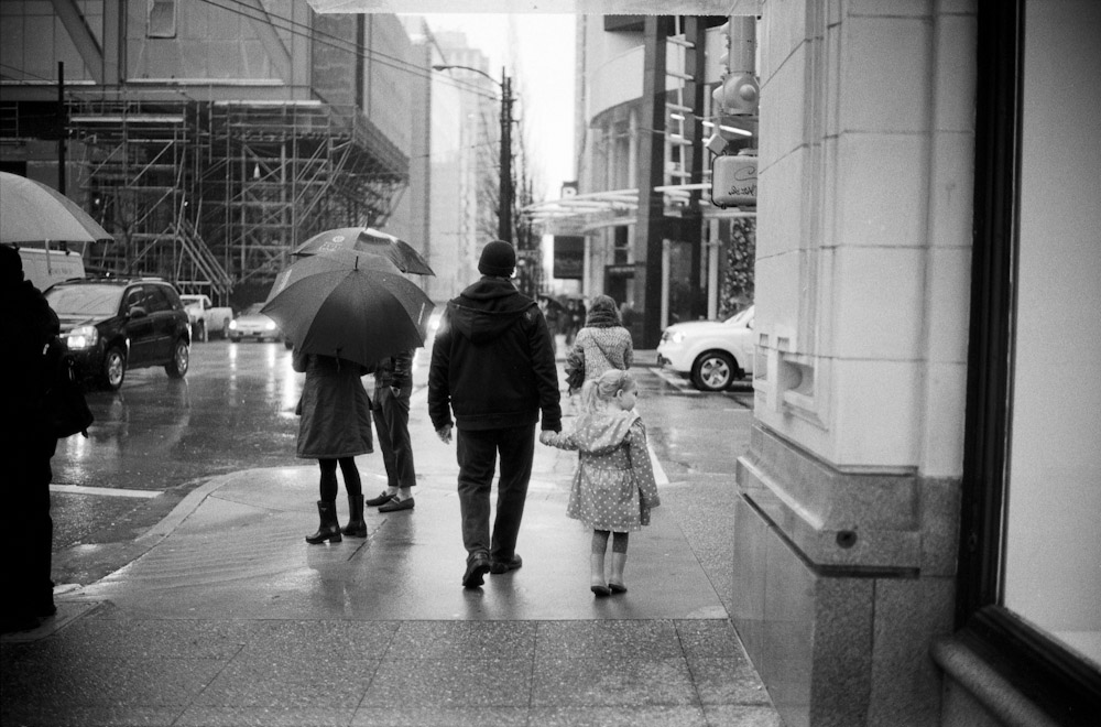 On this day, the rain was coming down lightly (thankfully). My camera was hidden under either it's case or something else but I was hastily walking when I saw these people. I had to quickly raise my camera, run forwards to wards them to try to frame them and get it all focused. 