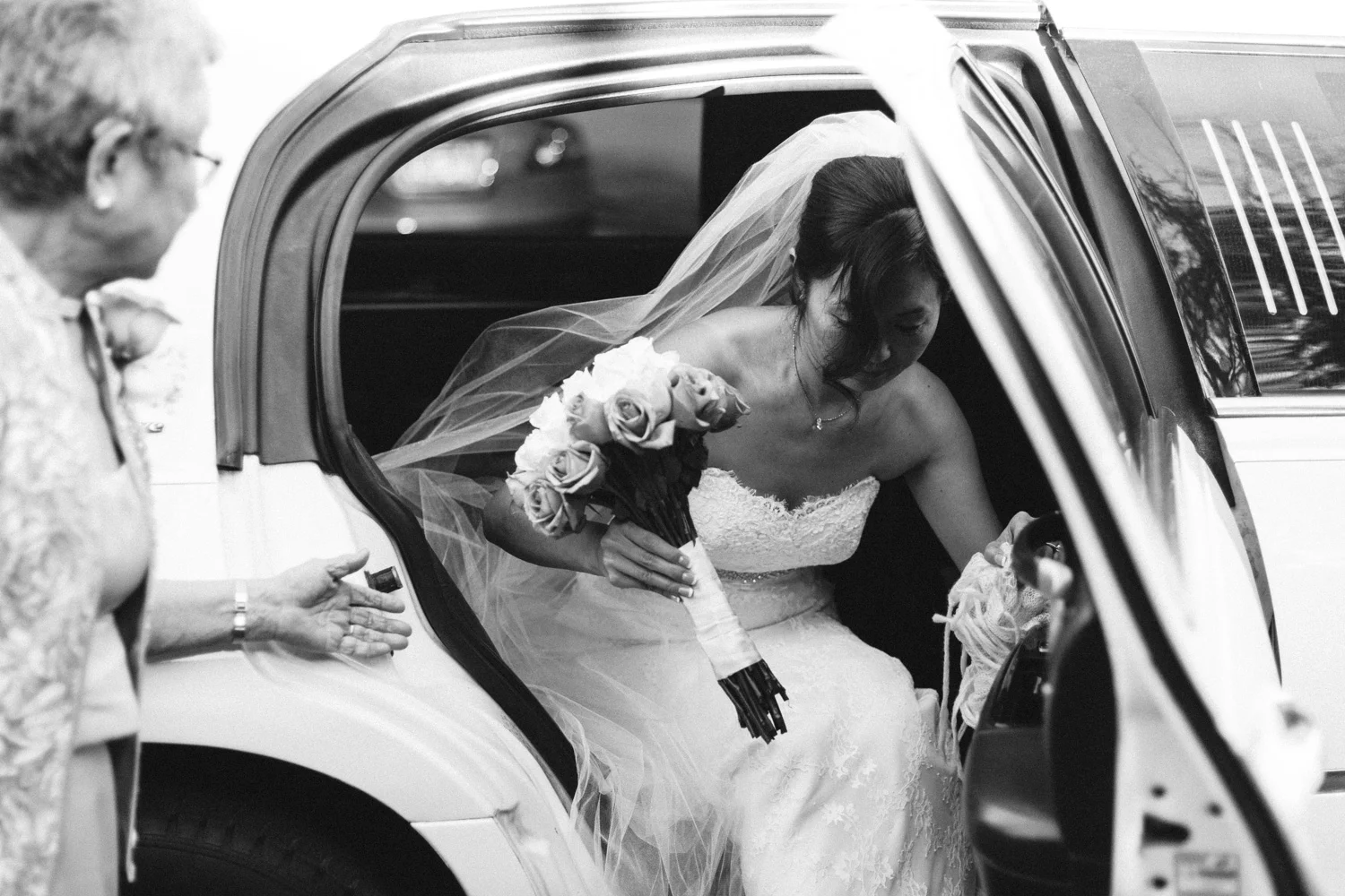 While I was photographing the groom inside the ceremony/reception area, I was keeping an eye on the door down the hall to see if a limousine would pull up. Eventually, it did and I was able to head out to the front door and document this moment of the bride making her way out of the limousine.