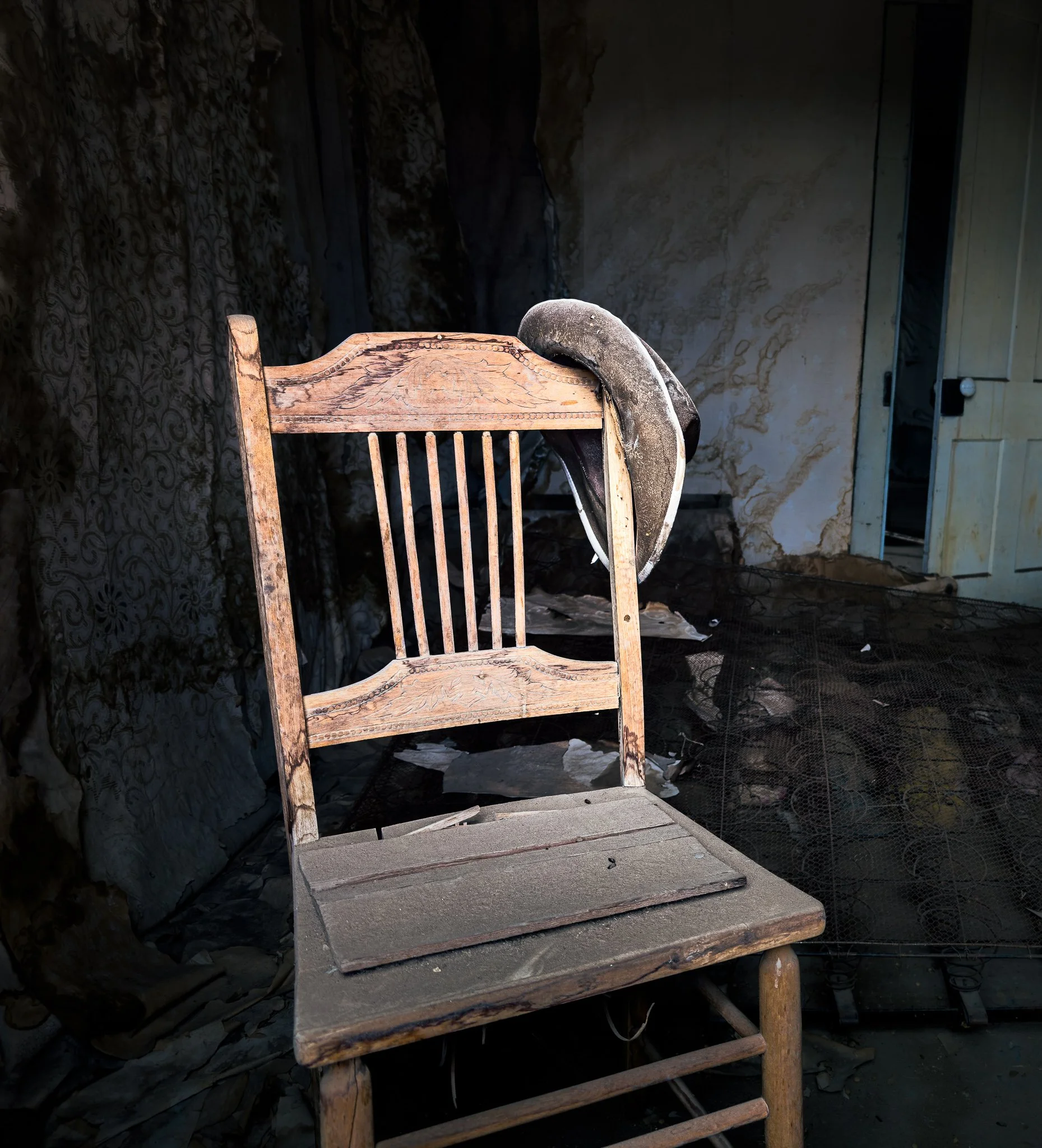 A worn wooden chair and weathered hat stand in a dim room at Bodie beside a dark doorway.