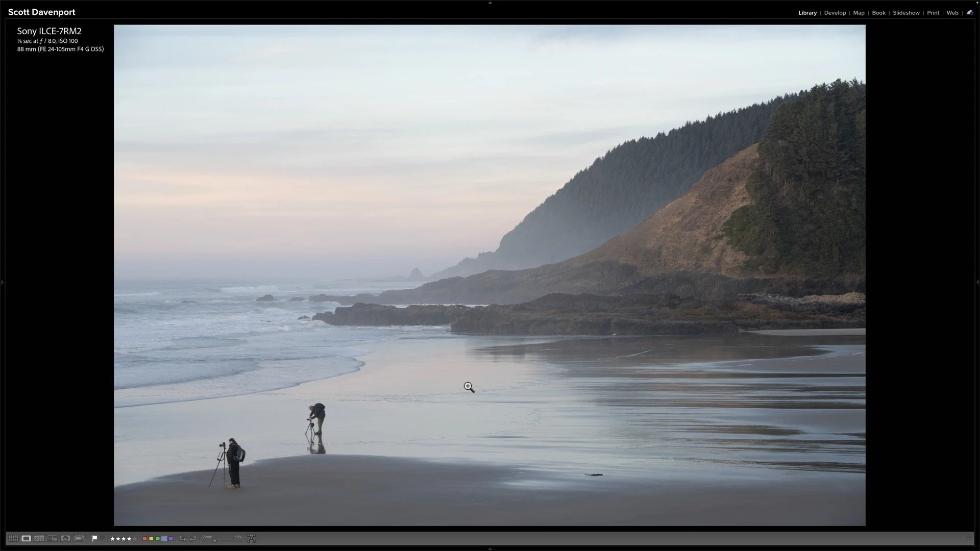 Photographers occupy the lower-left corner of a rocky coastal scene, facing toward the left edge beneath misty headlands.