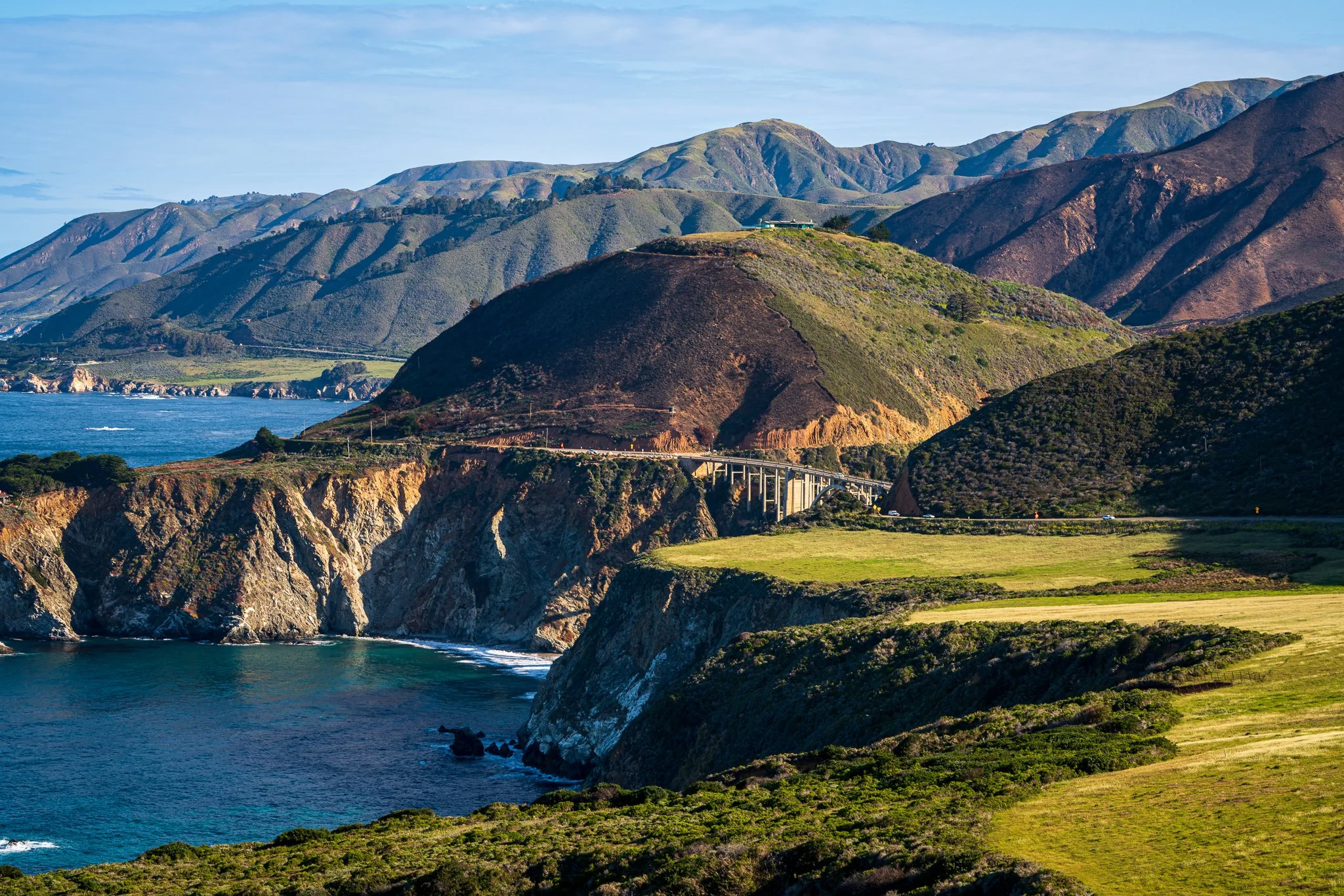 Bixby Bridge and Highway 1 cross layered green and brown headlands above the blue Pacific on the Big Sur coast.