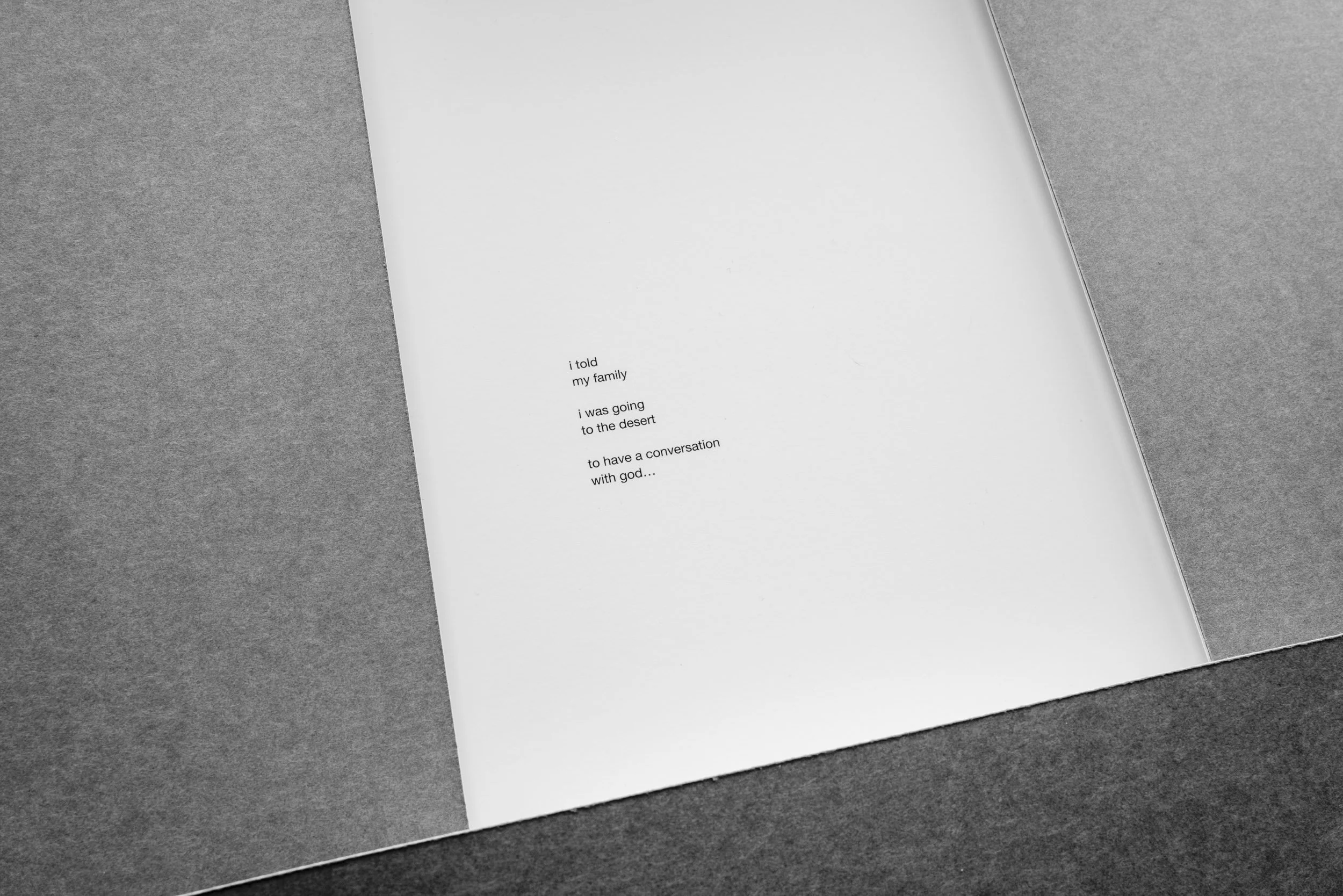 A white sheet of paper with typed text is placed diagonally on a gray surface. The text reads: "i told my family i was going to the desert to have a conversation with god...".