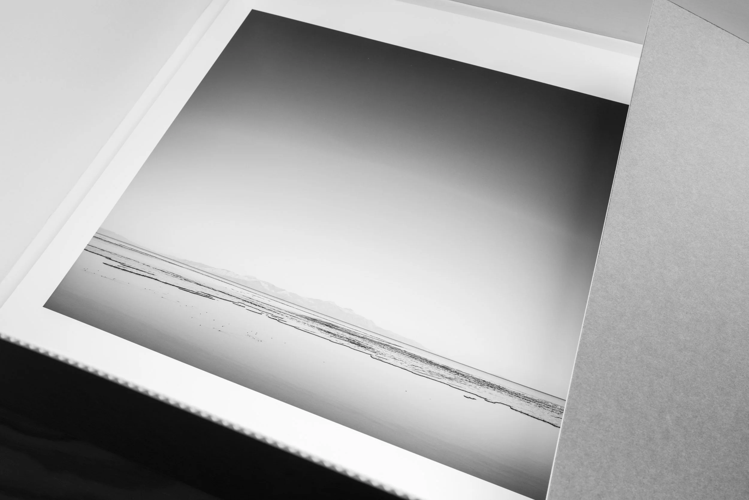Close-up of an open photo album with black-and-white landscape photos on white pages, framed by a gray cover.