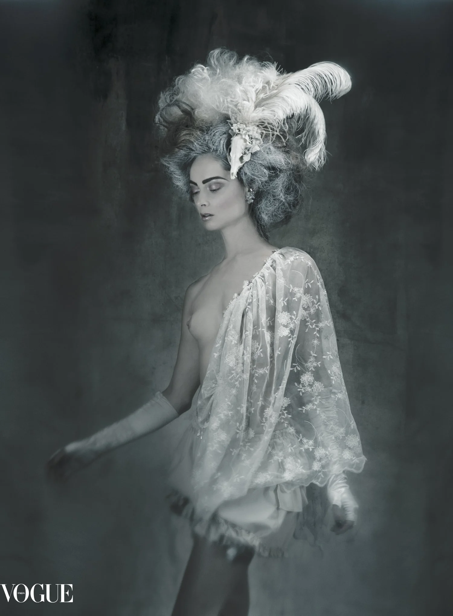 A woman with elaborate white feather and floral headpiece, styled in a vintage fashion, wearing a sheer embroidered lace shawl, standing against a dark background with a misty atmosphere.