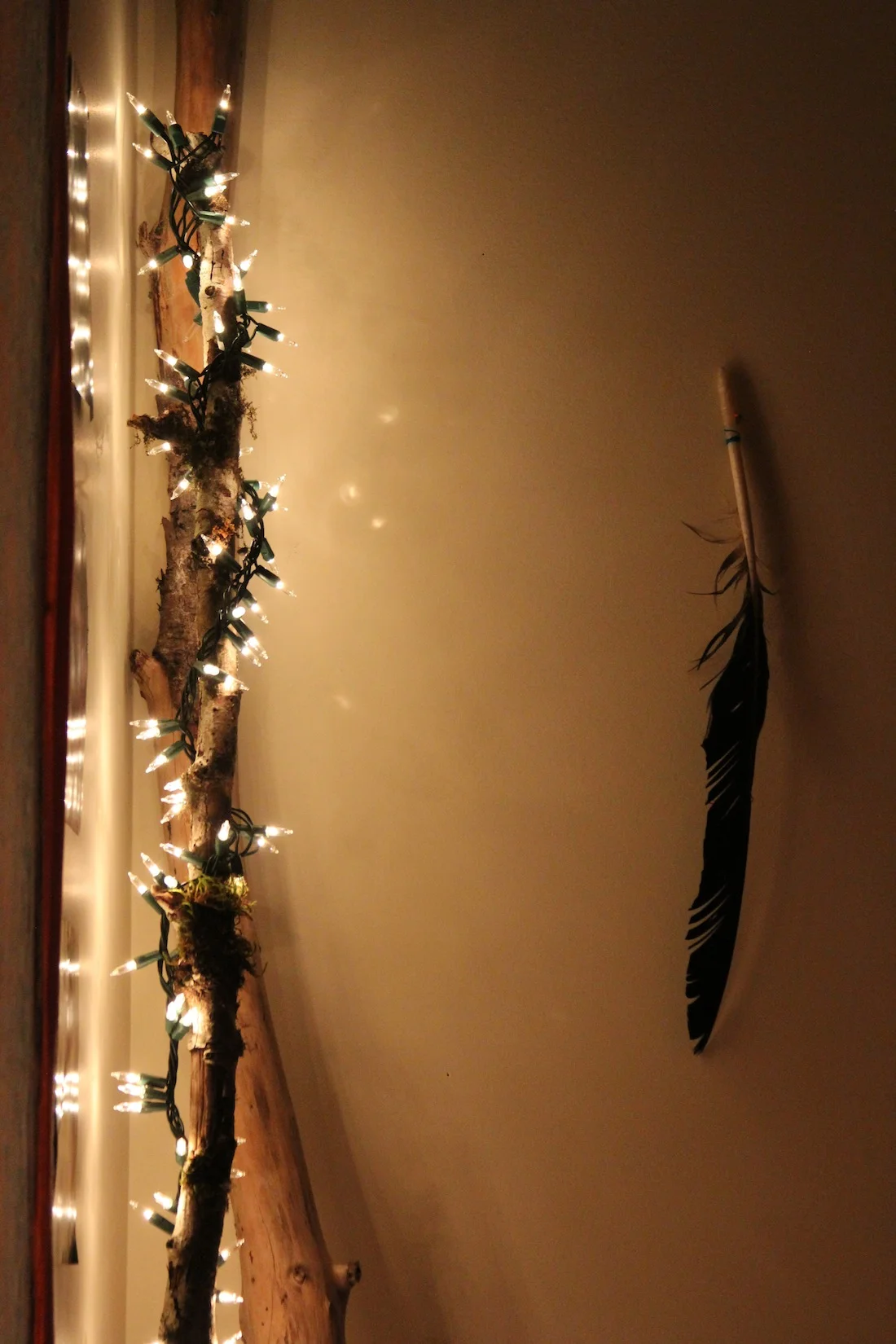 An eagle feather hangs beside a DIY lamp - twinkling lights wrapped around a long piece of wood!
