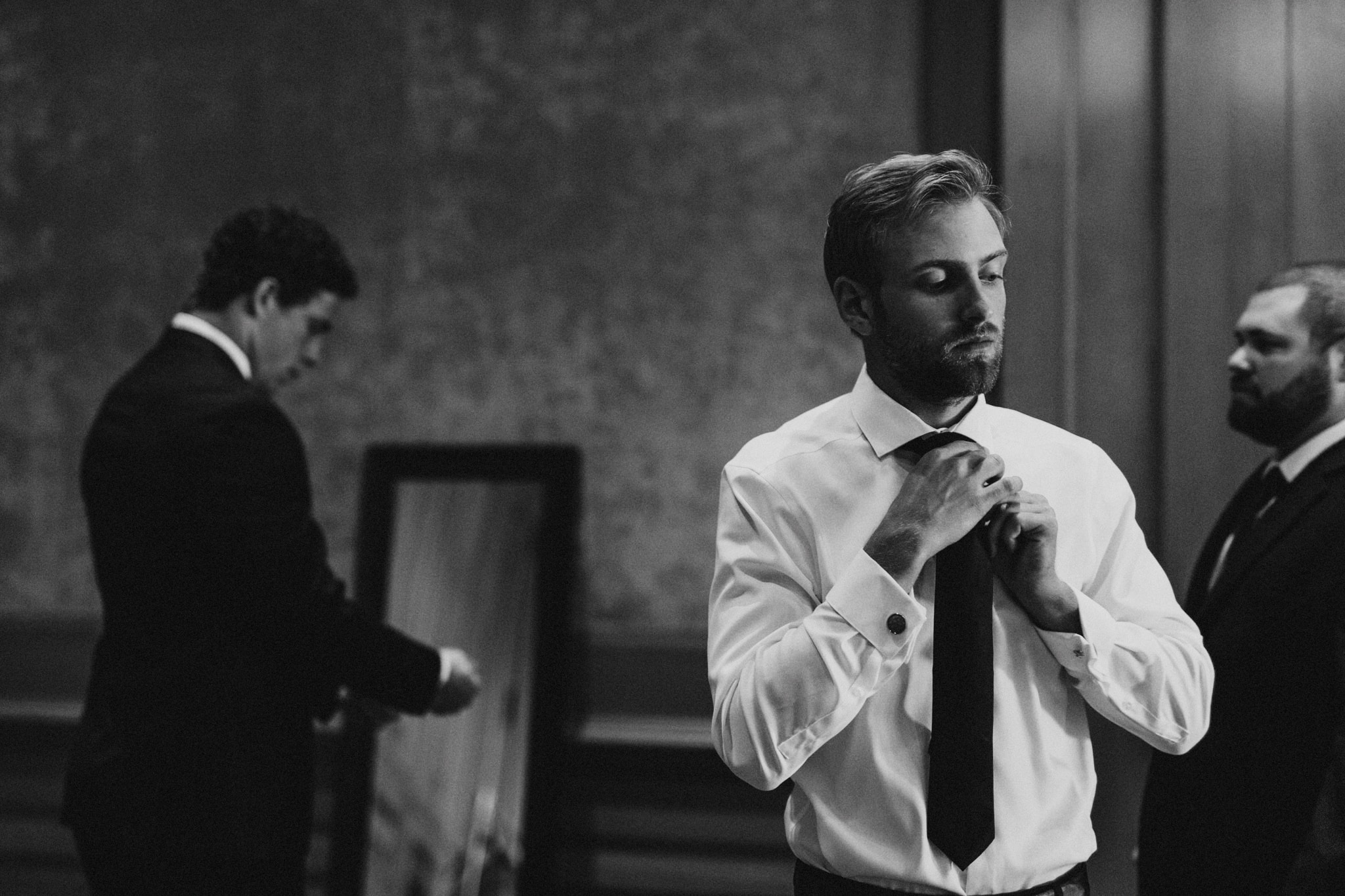 A groomsman tightens his tie in a room at The Resort at Pelican Hill while getting ready for a Newport Beach wedding.
