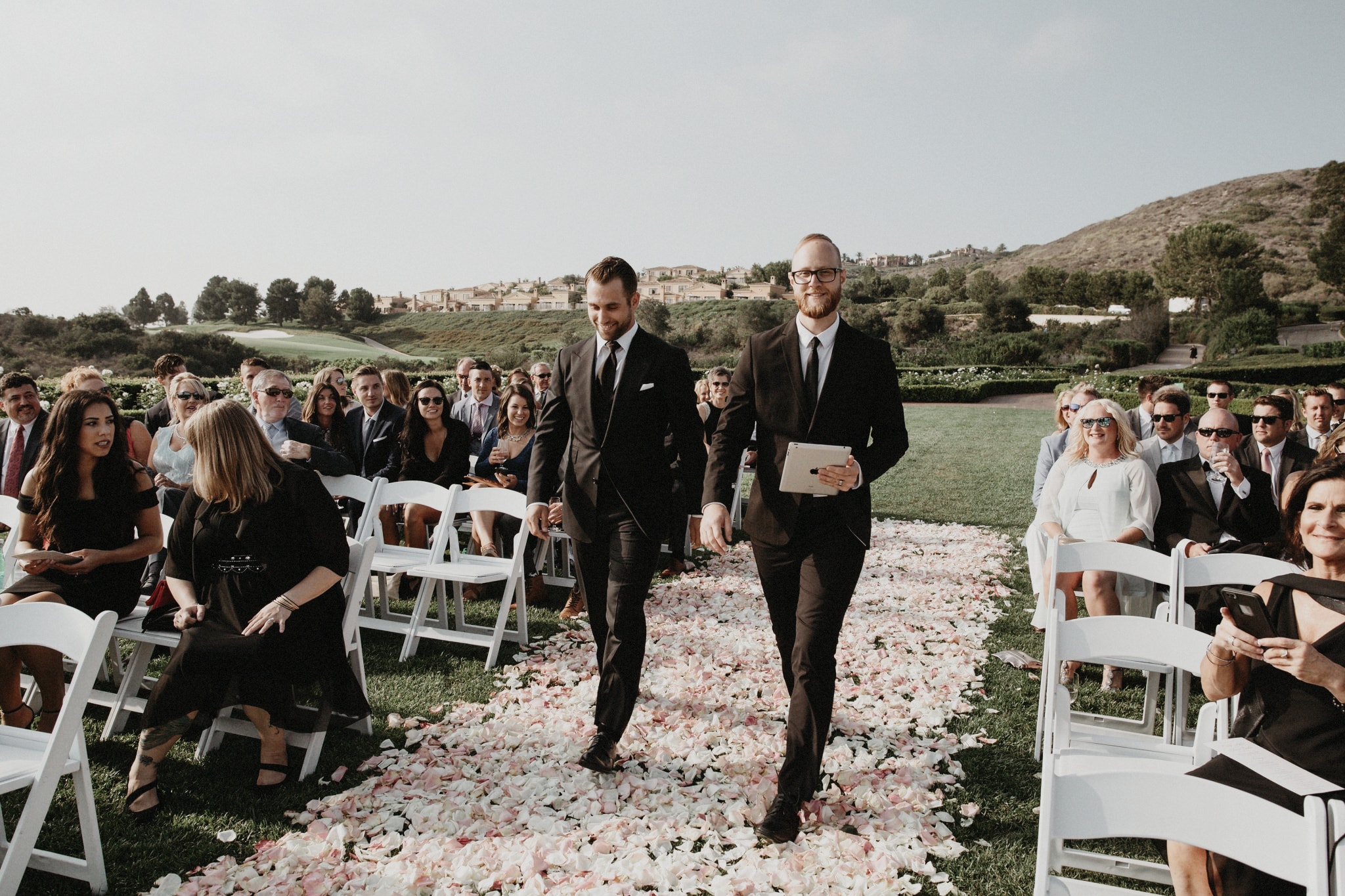 The groom walks down the aisle during a beautiful outdoor ceremony in Newport Peach, California.