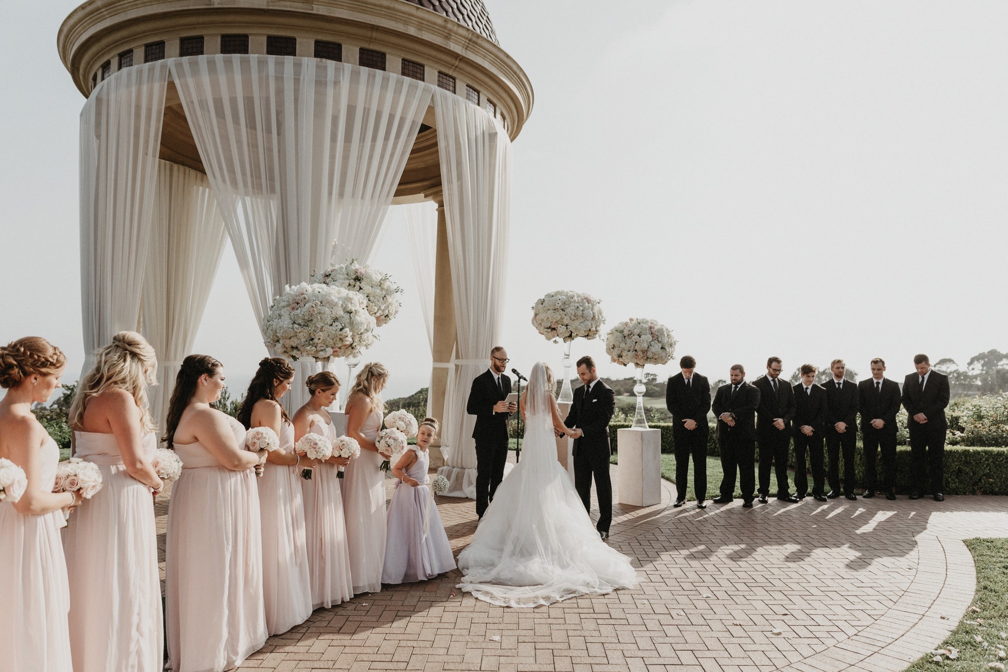 Bridesmaids in blush pink dresses watch as the bride and groom exchange their vows at a Newport Beach wedding ceremony.