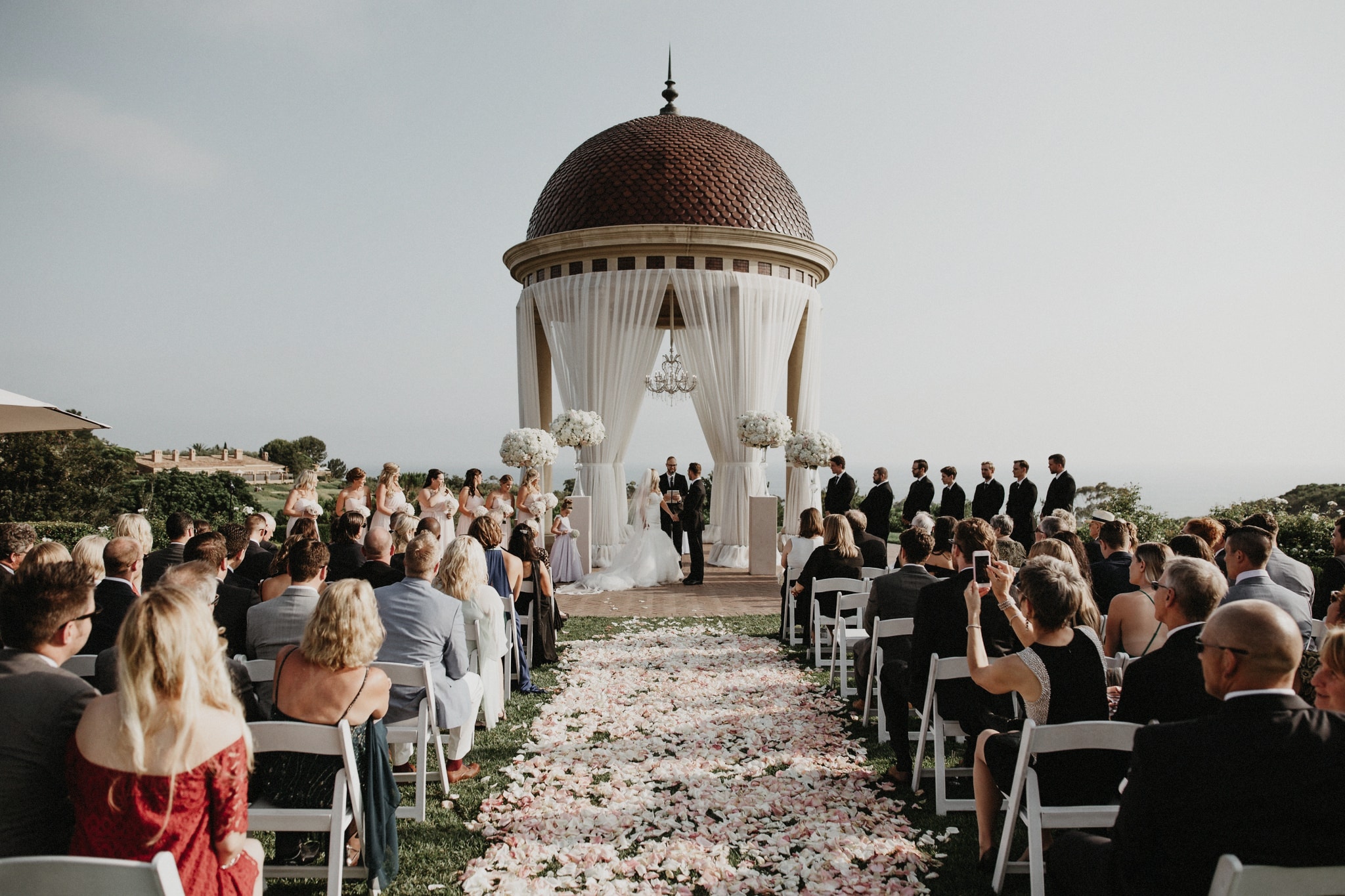 Guests watch as a bride and groom exchange vows in front of a beautiful alter at an outdoor wedding ceremony in Orange County.