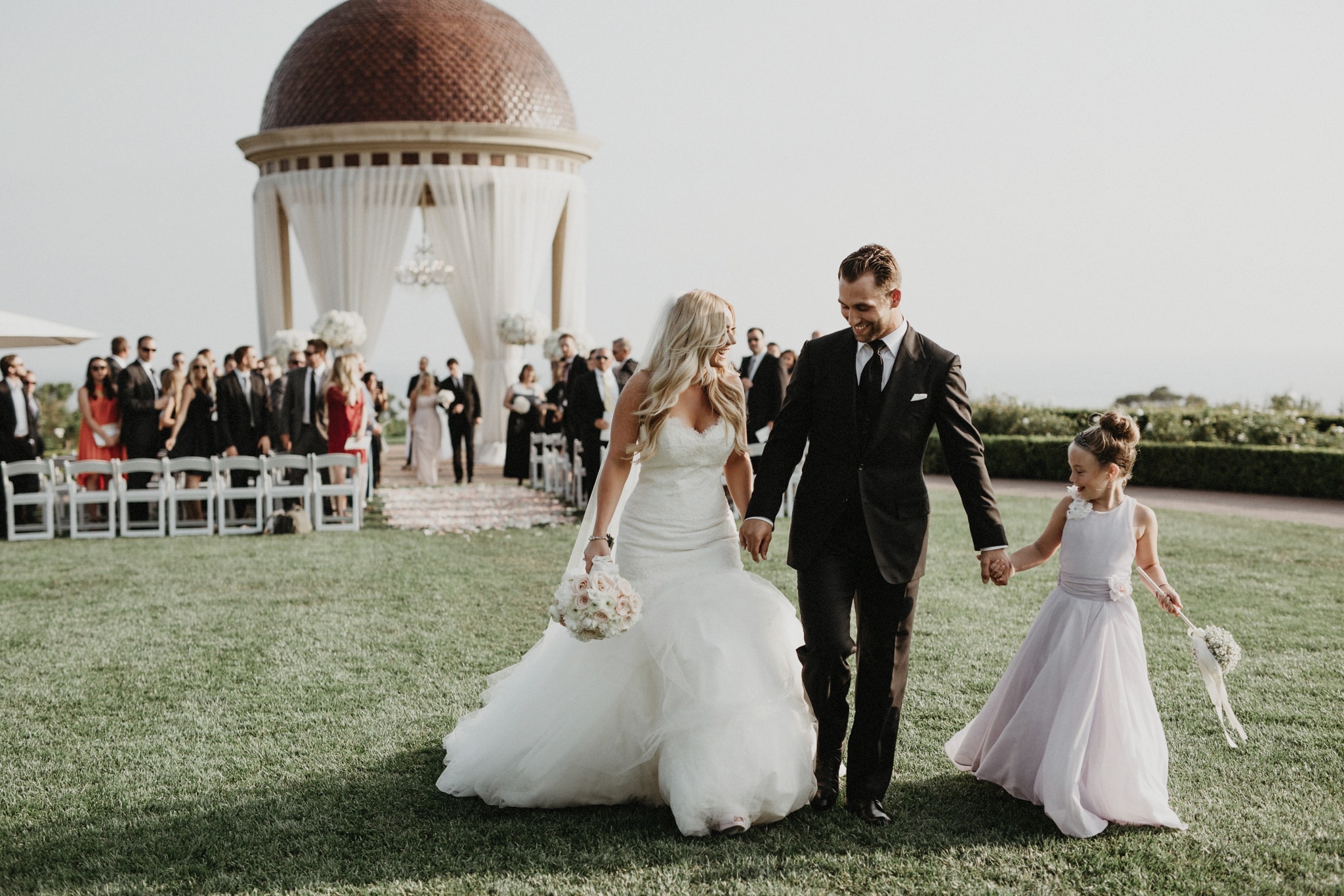A bride, groom, and flower girl walk hand in hand together at a beautiful Newport Beach wedding at The Resort at Pelican Hill.