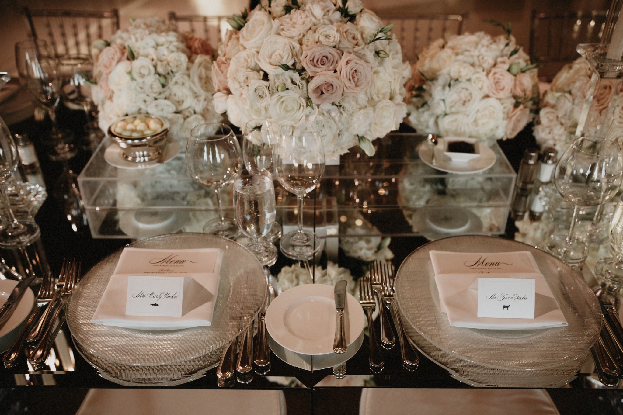 Wedding table settings at Pelican Hill Resort including beautiful bouquets of pink and white roses, white plates, and crystal glassware.