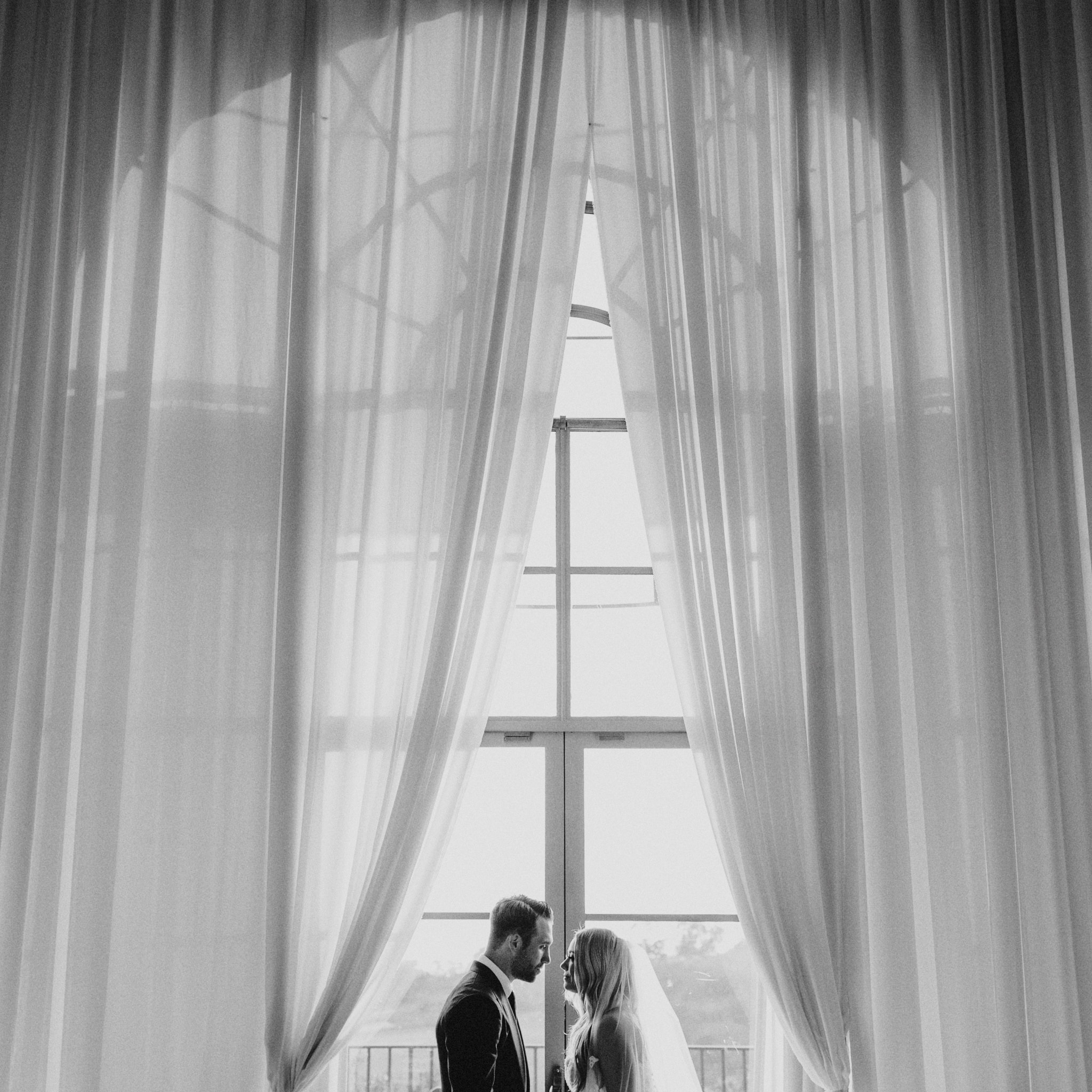 A newlywed bride and groom stand, looking at each other, in front of a window during their wedding at Pelican Hill Resort.