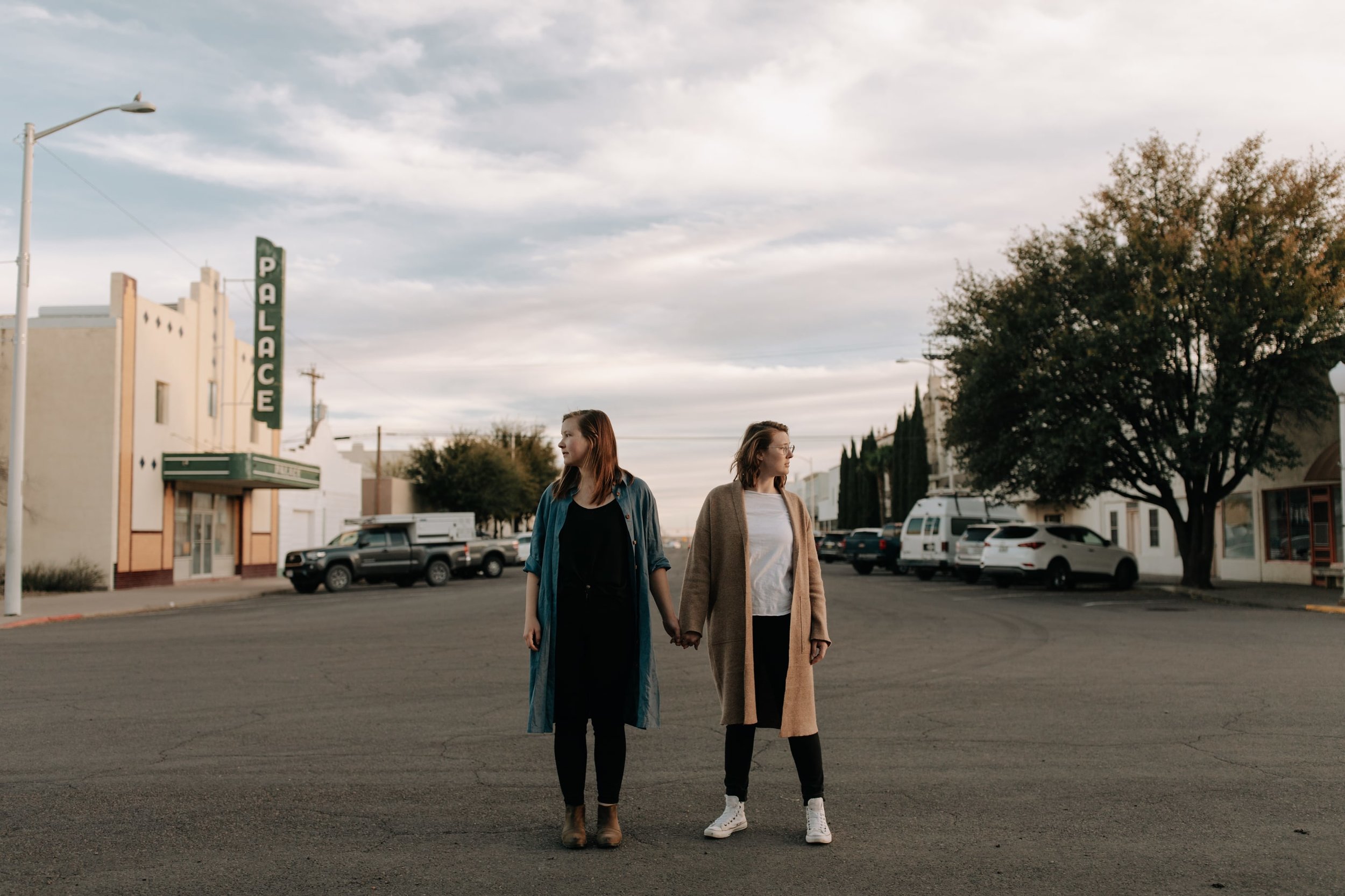 A couple wearing casual clothes stand holding hands and looking away from each other in the street in Marfa, Texas.