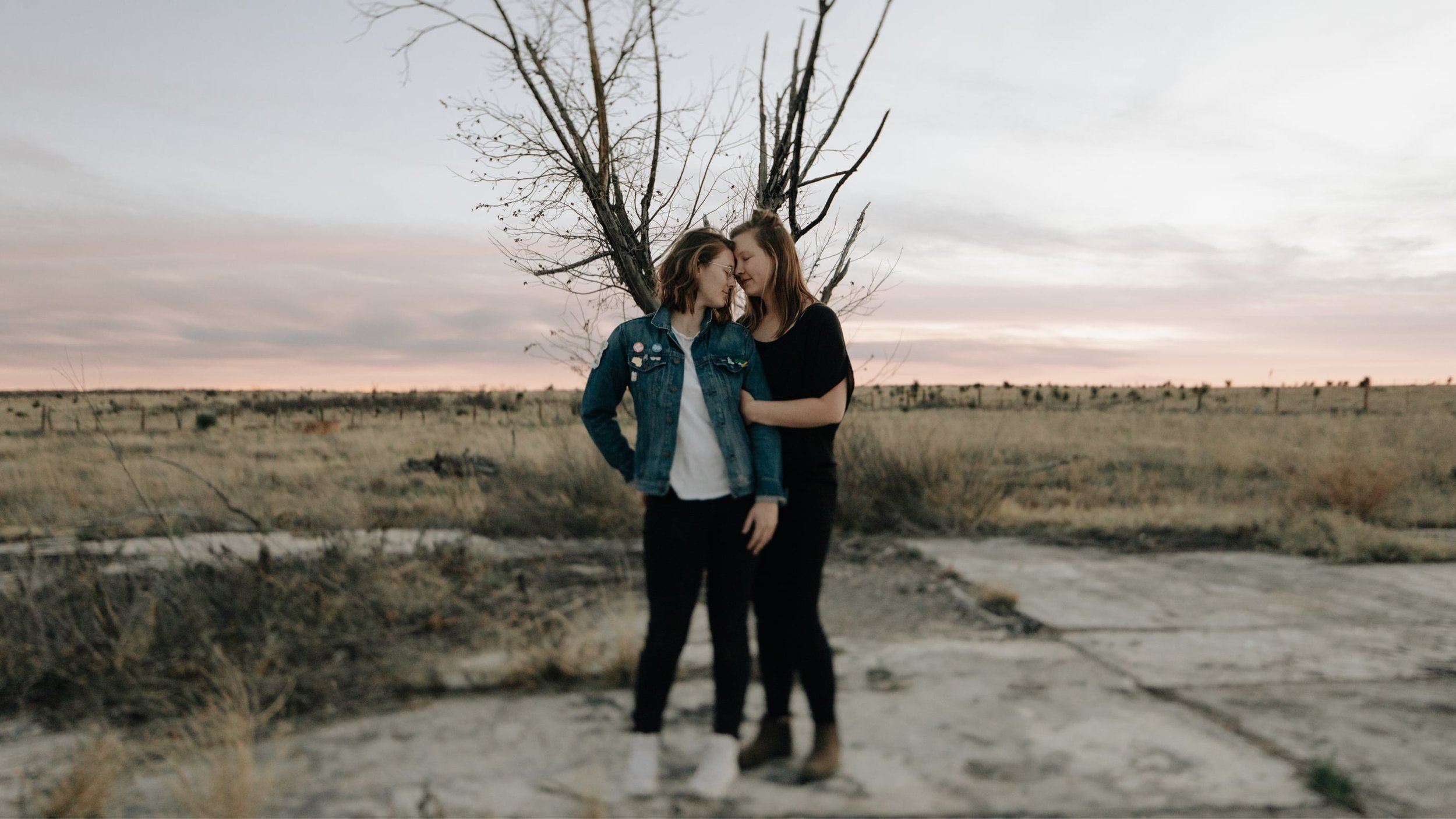 Two women in love stand together in a field in Marfa, Texas, near the El Cosmico Hotel.