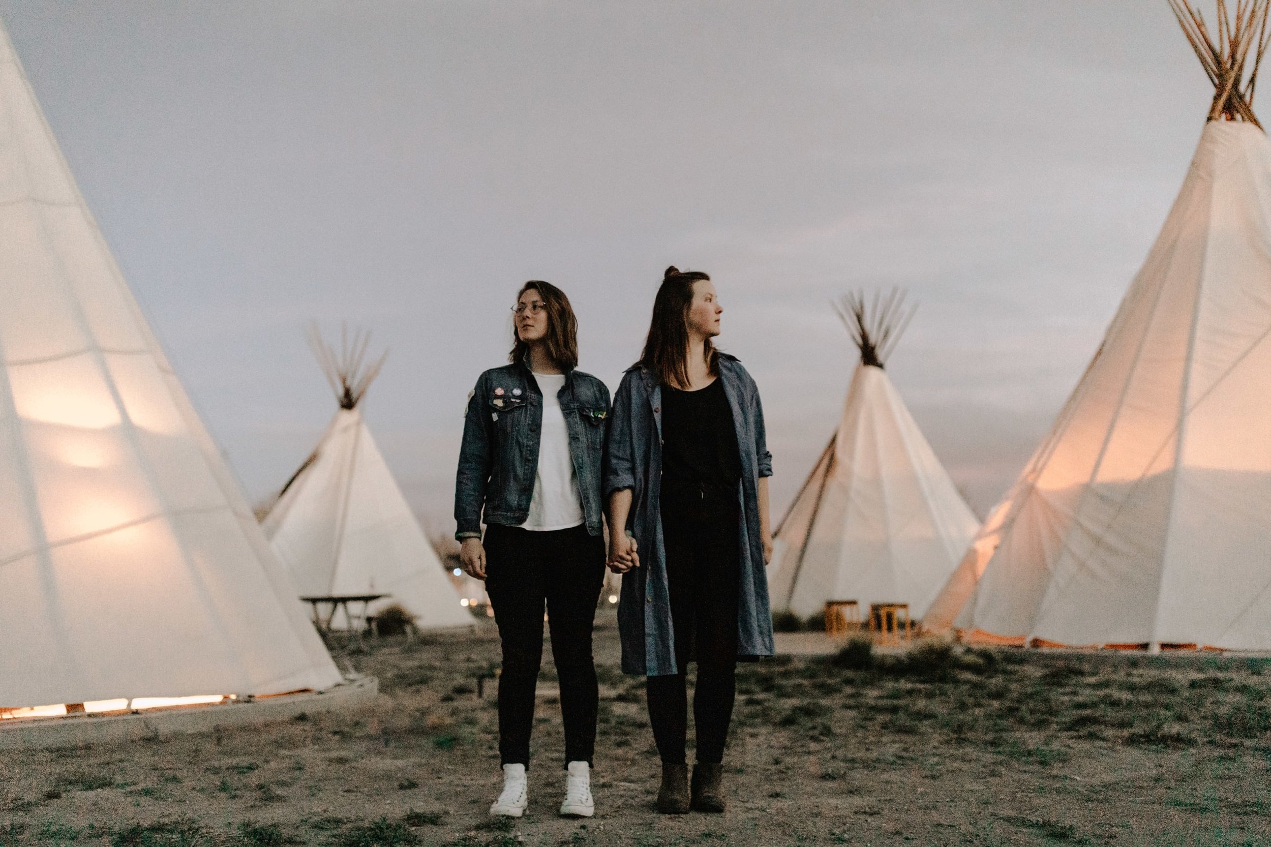 A couple holds hands and looks in opposite directions amongst tents at the El Cosmico Hotel in Marfa, Texas while photographer Josh Olson captures the moment.