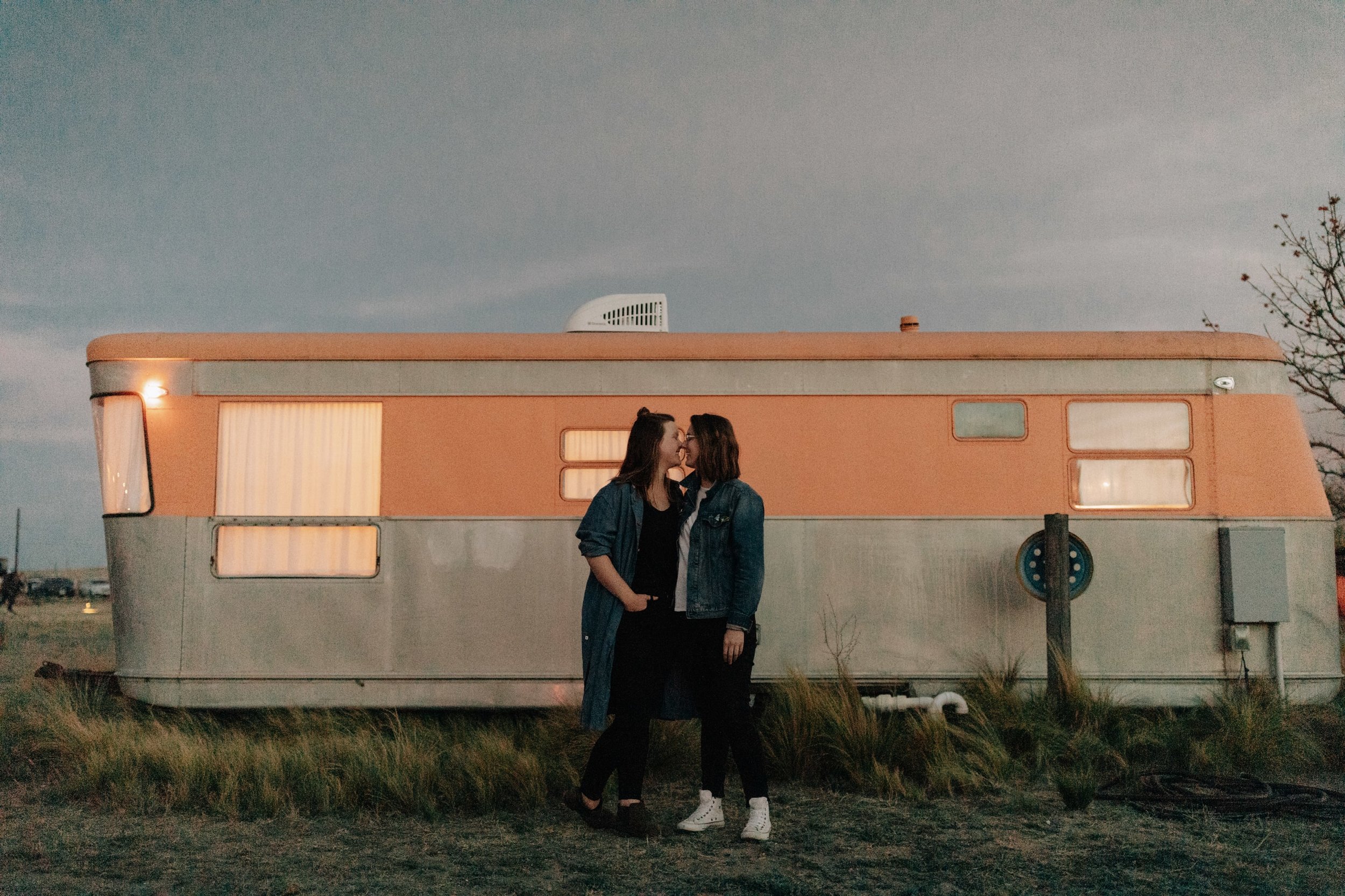 A couple smiles at each other in front of a trendy trailer at the El Cosmico Hotel in Marfa, Texas.