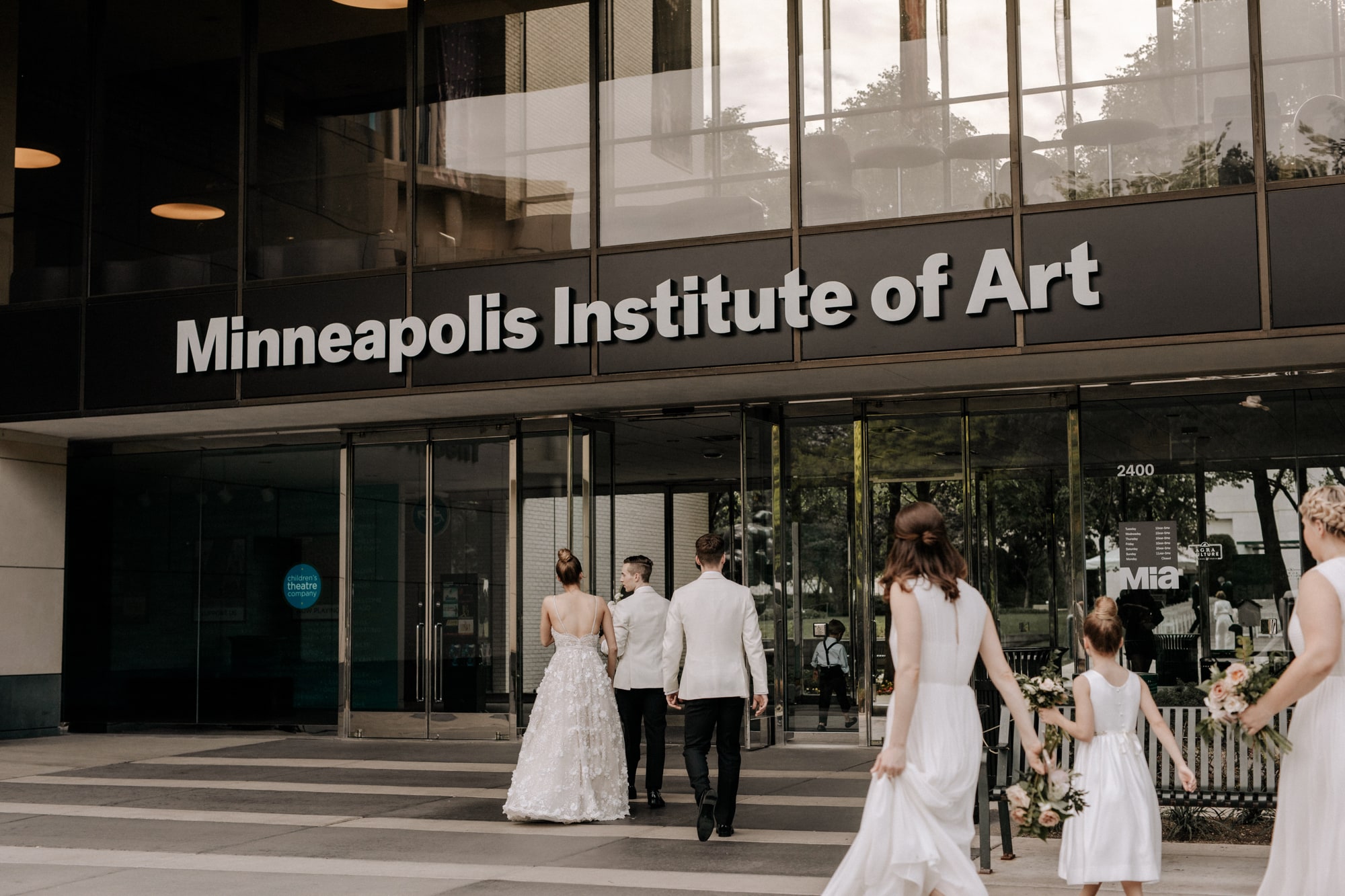 A bride and groom walking into the Minneapolis Institute of Art, following by their wedding party, during a beautiful wedding captured by Minneapolis wedding photographer Josh Olson.