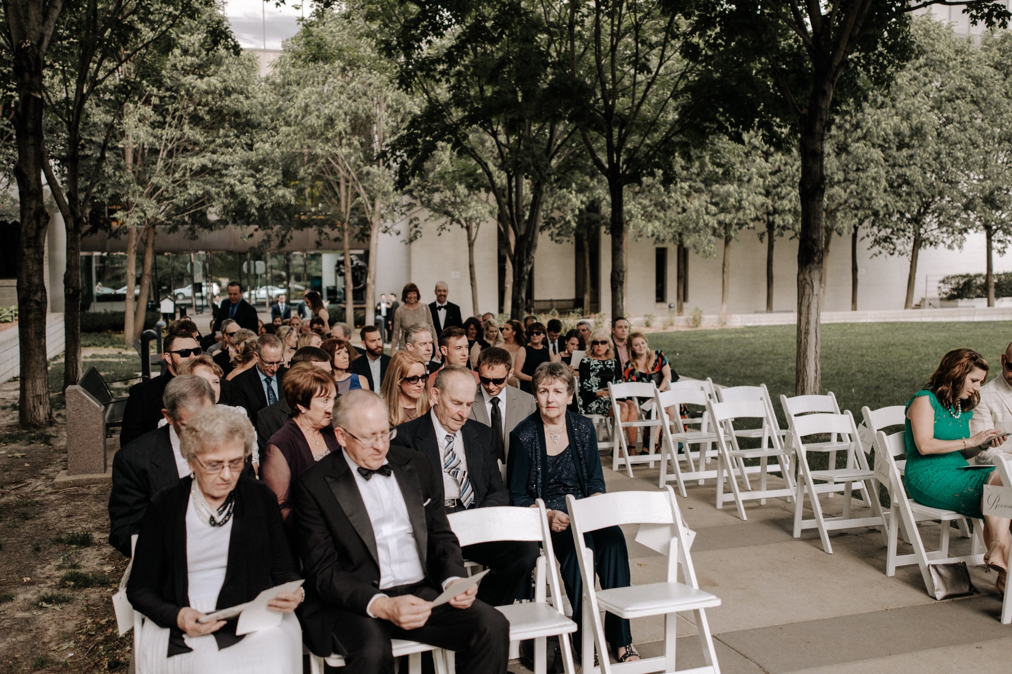 Guests sit in white chairs awaiting the bride and groom during an outdoor wedding ceremony at the Minneapolis Institute of Art, capture by j.olson weddings.