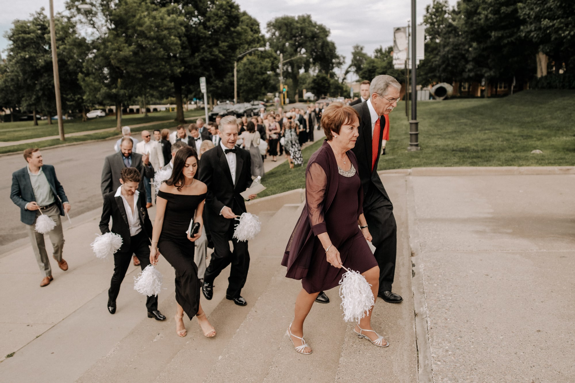 Wedding guests hold white pom poms while walking up the steps to the Minneapolis Institute of Art.