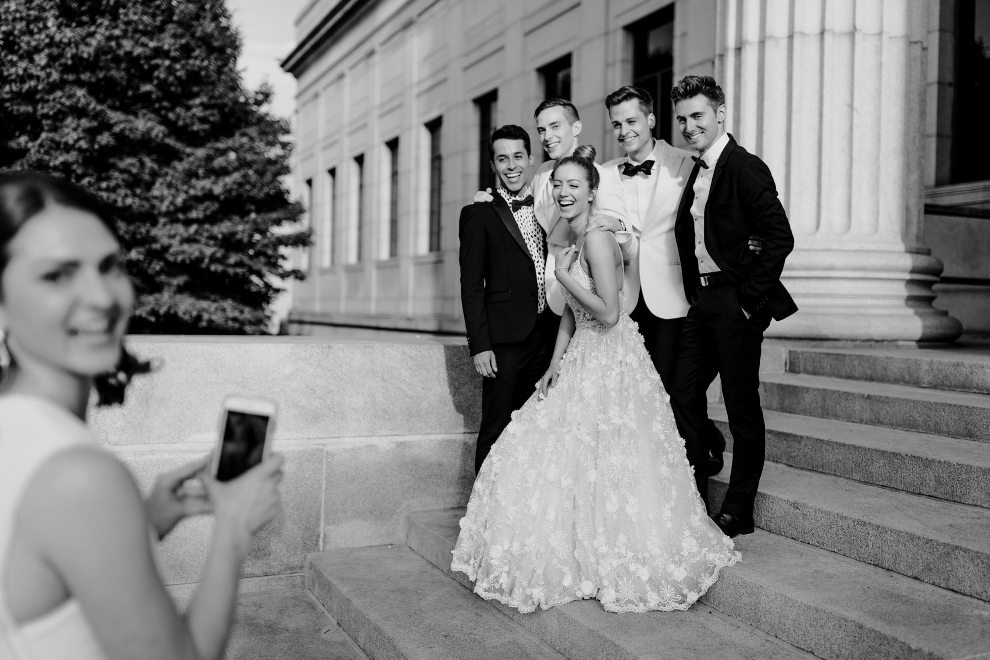 A bride laughs while posing with the groomsmen for wedding photos with Josh Olson Wedding Photographer outside of the Minneapolis Institute of Art.