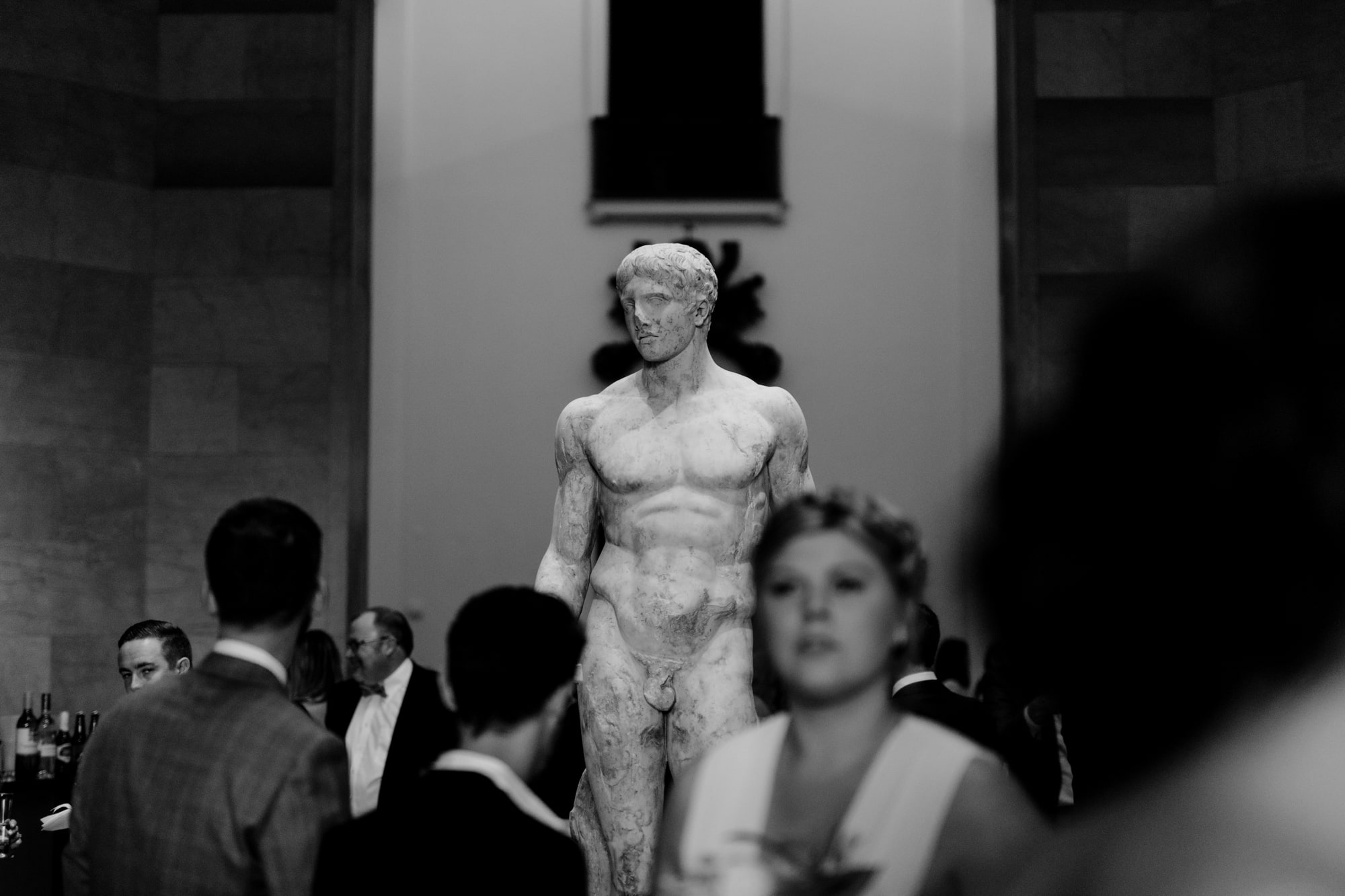 Wedding guests mingle in the Minneapolis Institute of Art, around a large statue of a man.