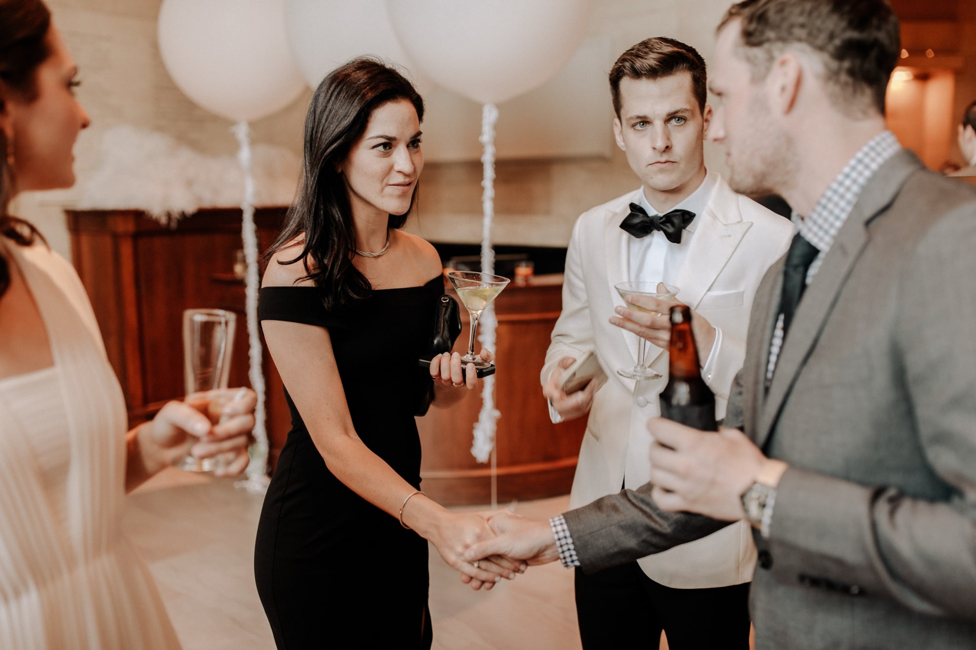 A beautiful woman in a black dress stands beside a man in a white tux while mingling with guests at a Minneapolis Institute of Art wedding.