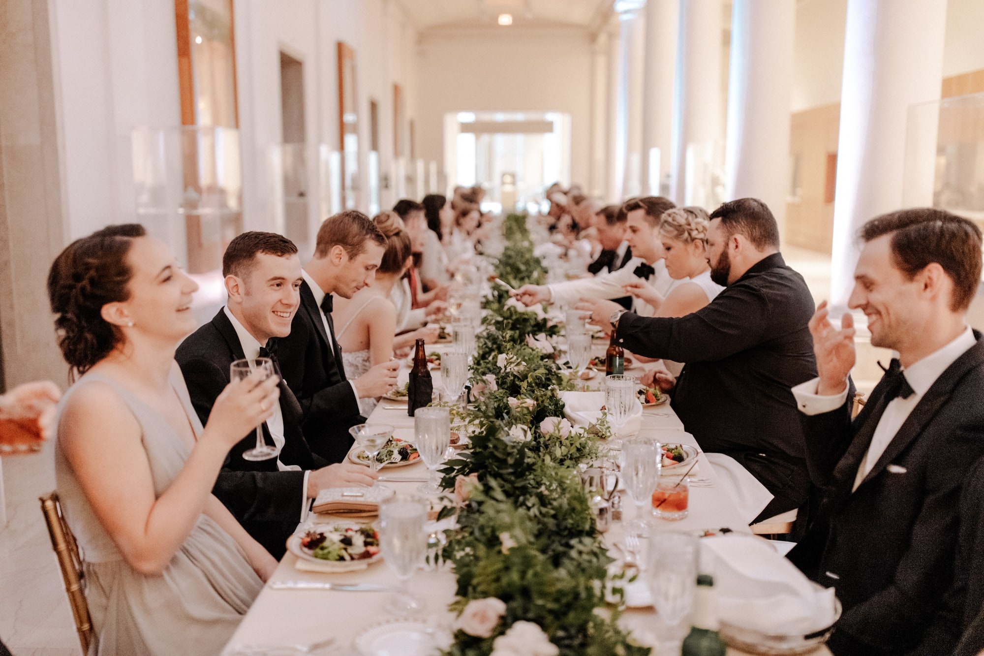 Well-dressed guests sit at a long table during a wedding reception dinner inside the Minneapolis Institute of Art.