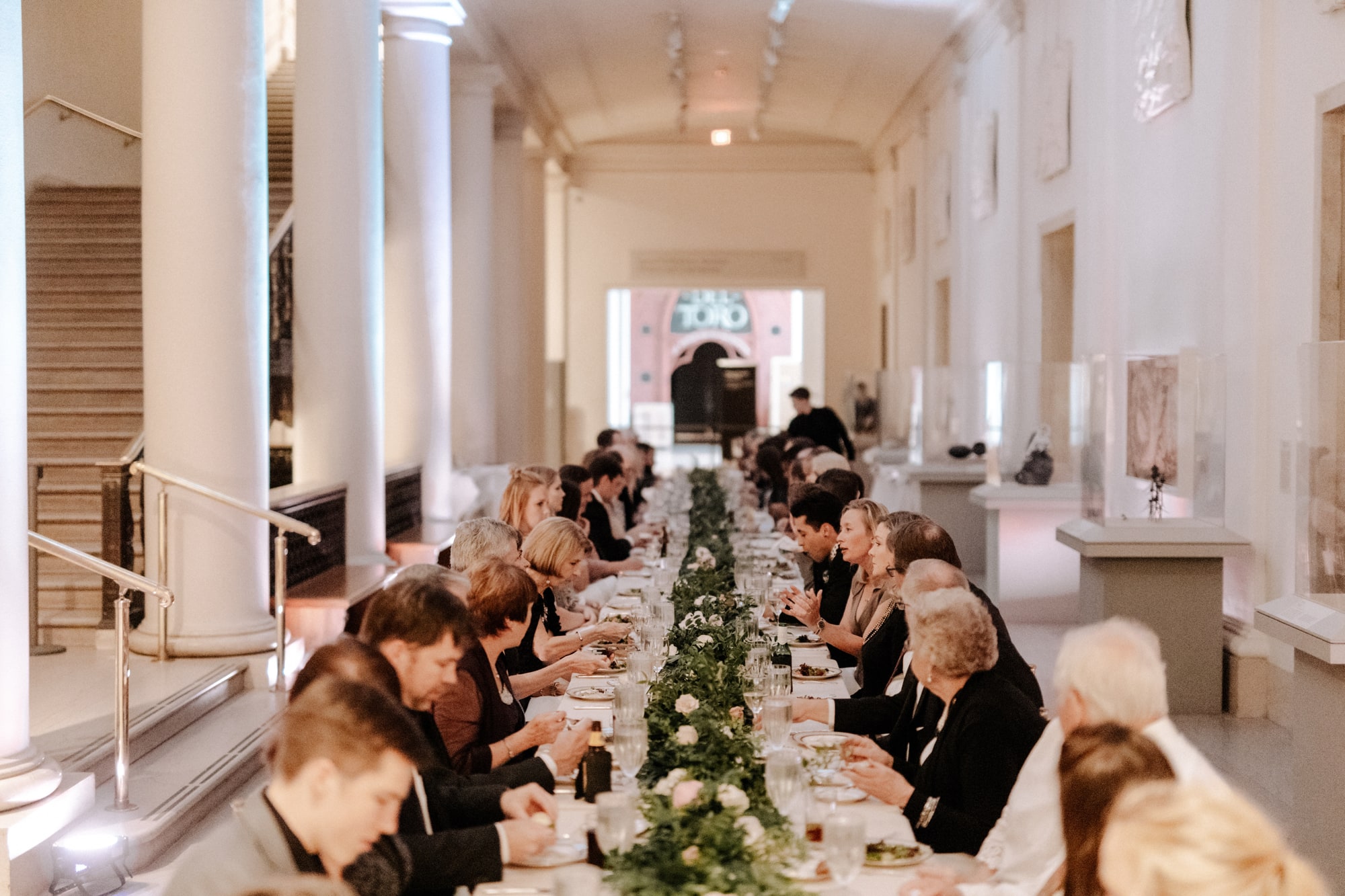 Guests enjoy a meal at a long, well-decorated table during a beautiful wedding inside the Minneapolis Institute of Art.
