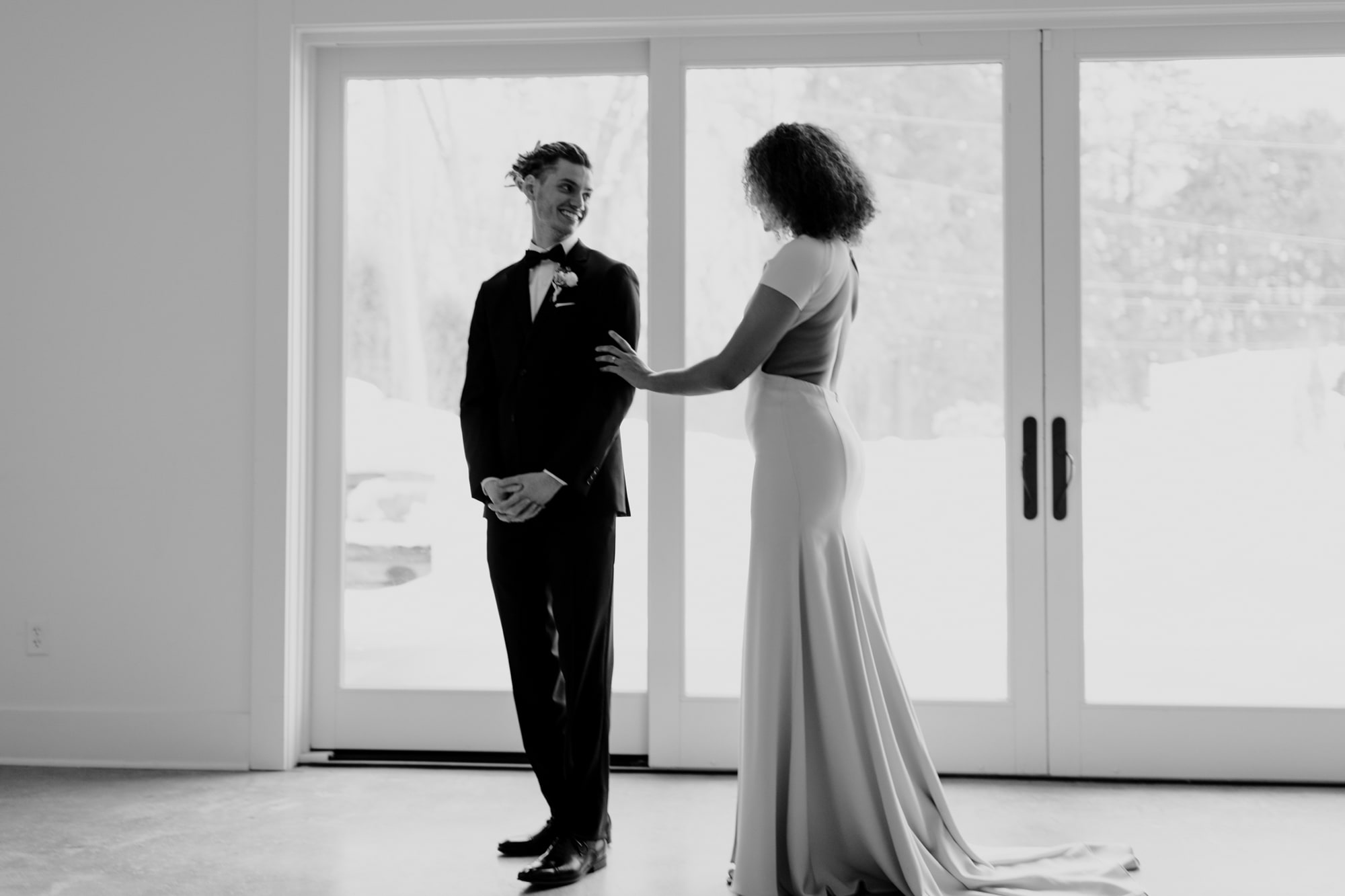 A bride in a beautiful backless dress touches her groom on the arm during their first look at their Minneapolis wedding.