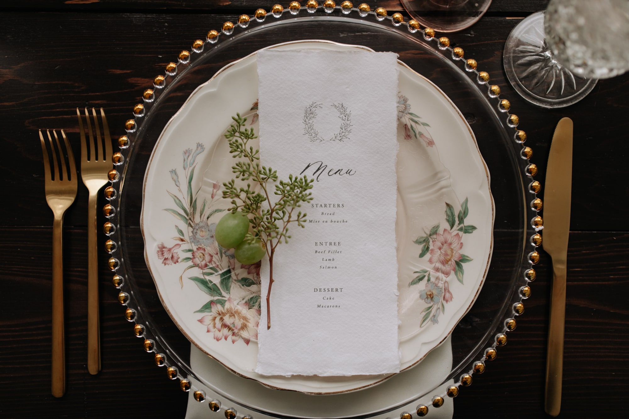 A wedding table setting with gold cutlery, a plate painted with florals, and an elegant menu at Hutton House in Minneapolis.