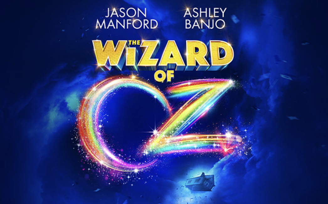 Poster do filme 'O Mágico de Oz' com nomes dos atores Jason Manford e Ashley Banjo, título em destaque e um arco-íris brilhante formando uma leiden com estrelas e um fundo azul estrelado.