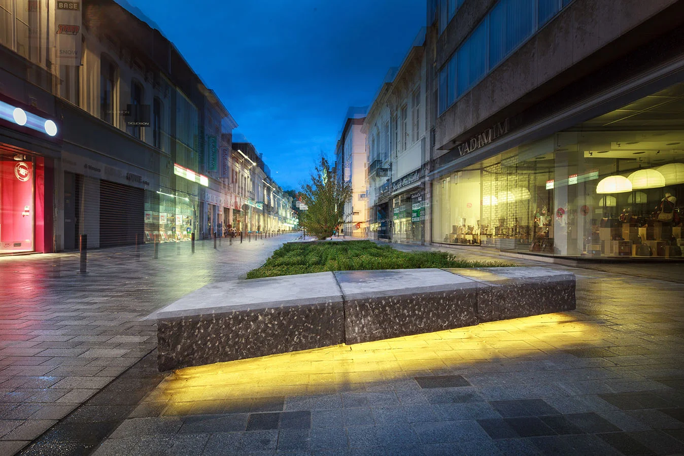 Nieuw aangelegde stationsstraat bij avond, foto van straatmeubilair, verlichting en beplanting.