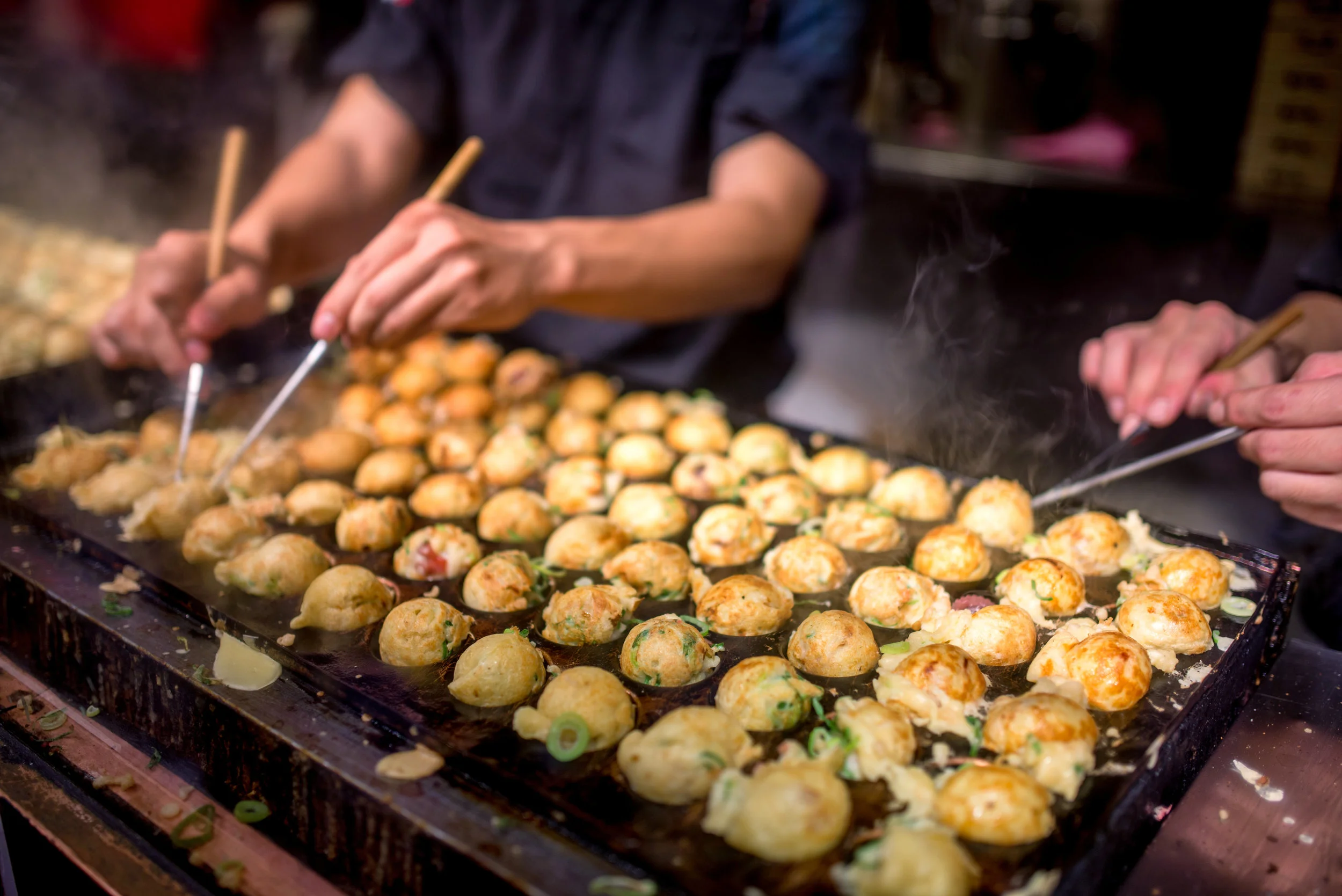 Takoyaki - a Kansai (Western Japan) favorite- savory balls of delicious, piping hot batter - being made on the grill.