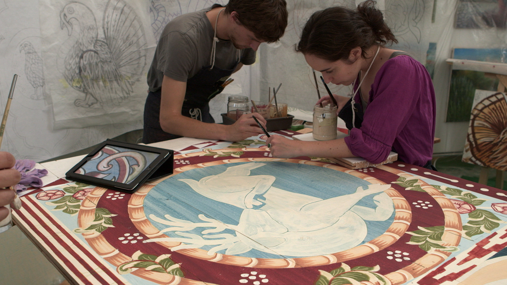 Still 24: Evelyn Tauben and Jason Bashaw paint the borders of the backward facing deer.