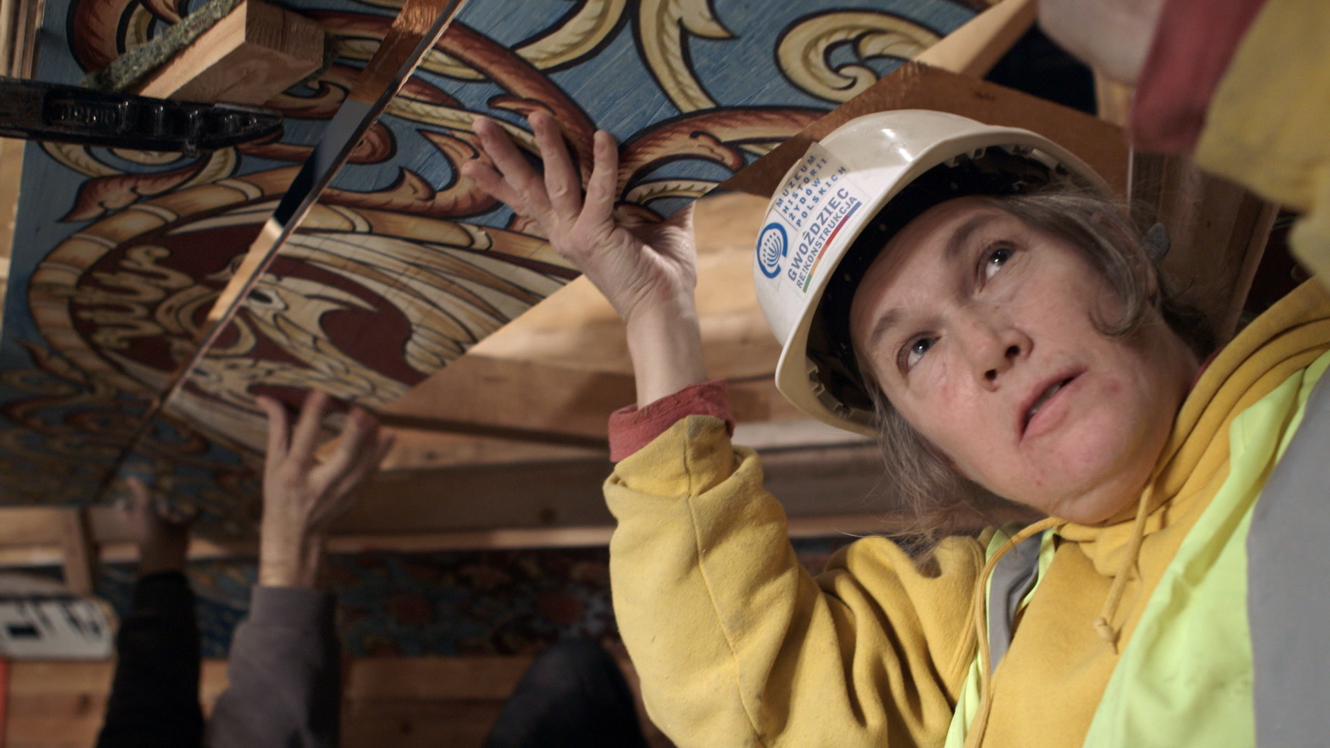 Still 38: Laura Brown installing a panel board during installation of the ceiling in the museum.