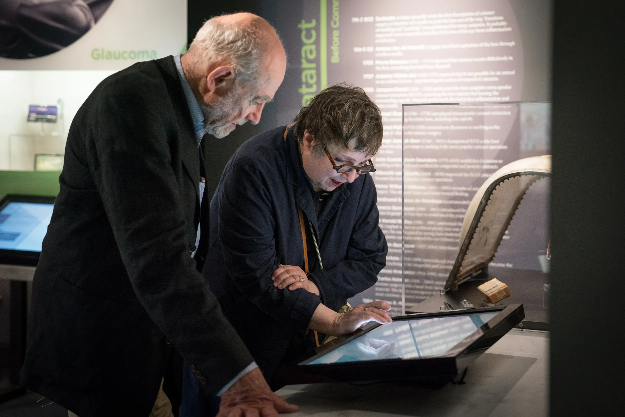 Two visitors use an interactive touchscreen beside a display of historical ophthalmic instruments at the Museum of the Eye.