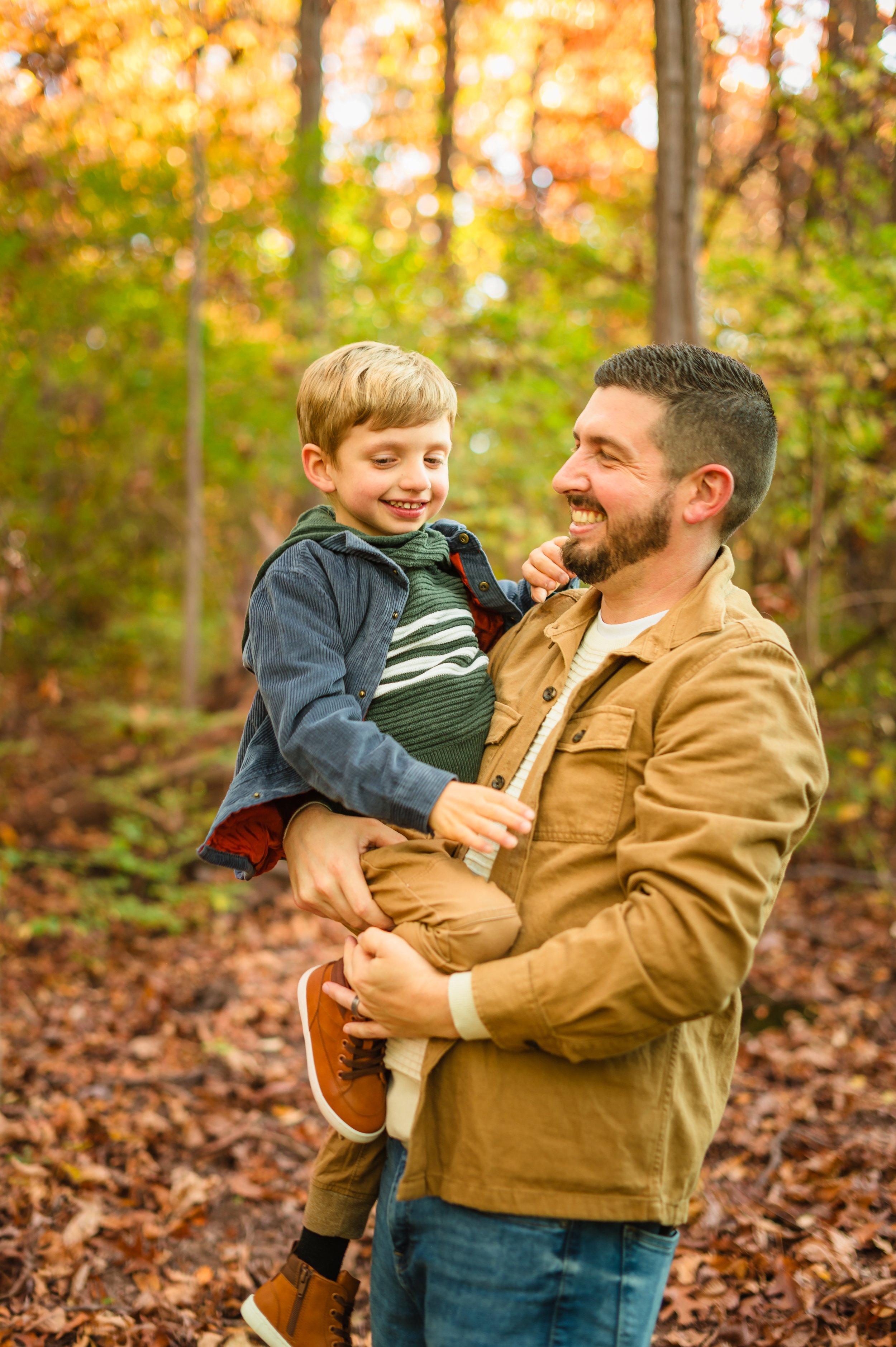 A man holding a smiling young boy in an autumn forest.