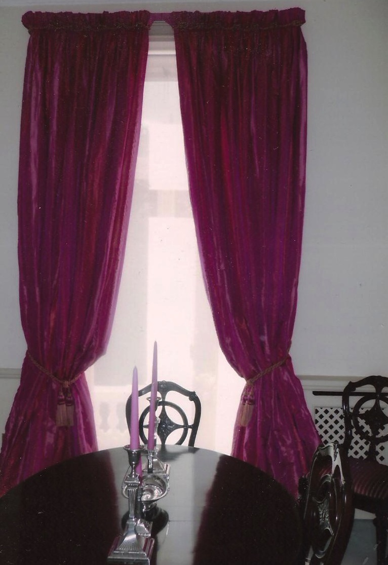 A rather bright pair of fuchsia pink curtains with rope trim and tassel tie backs and sheer roller blind in a town house in London