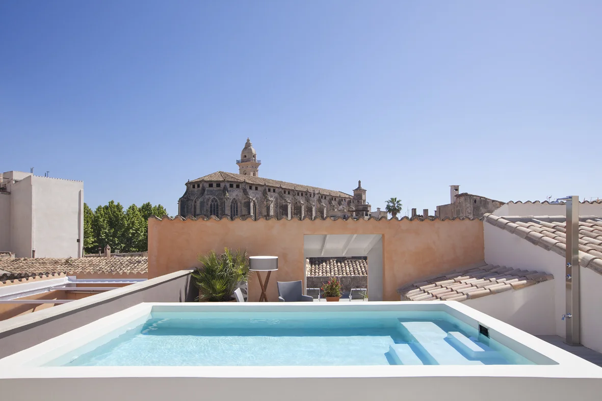 Heated rooftop pool area on the terrace with multiple sun loungers and seats to keep you comfy whilst sipping your favourite drink. Notice the Sant Francesc church in the background.