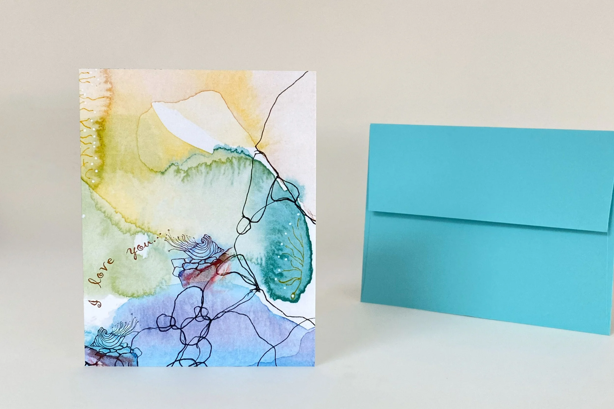 "I love you" front message Abstract watercolor greeting card featuring layered blue, green, and earth-tone artwork with expressive line drawing, shown with teal envelope