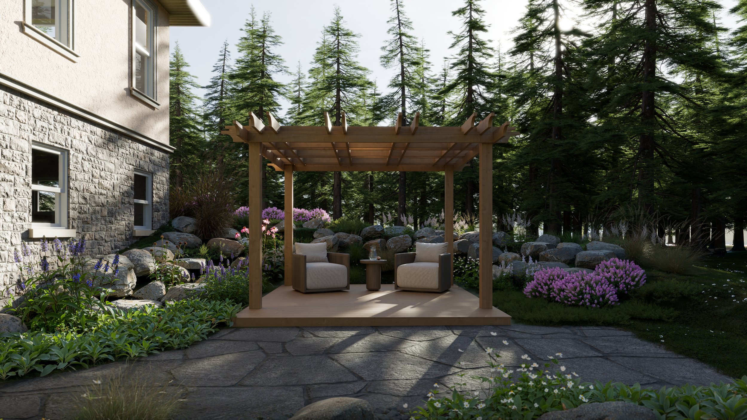 A backyard with a wooden pergola, two cushioned chairs, a small round table, and surrounded by colorful flowers and rocks, with a stone house wall and tall evergreen trees in the background.