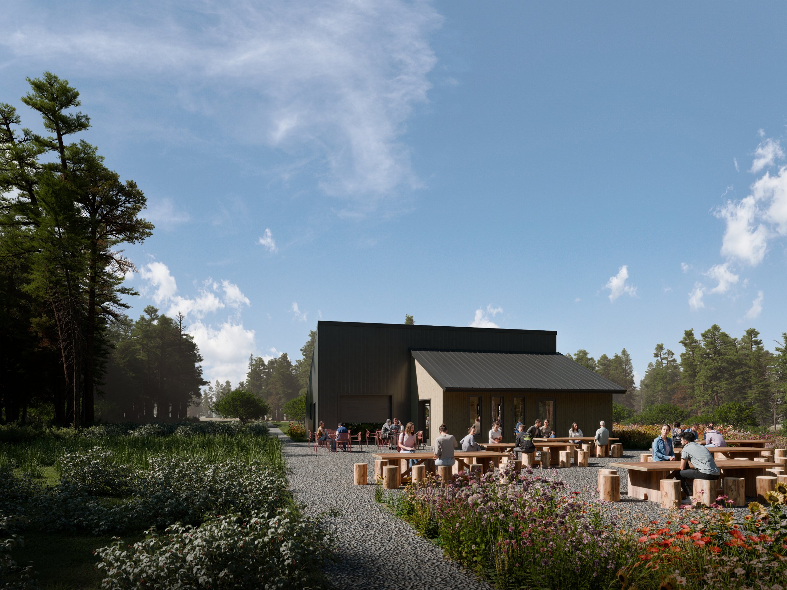 Outdoor gathering with people sitting at picnic tables in front of a modern building surrounded by greenery and trees, under a partly cloudy sky.