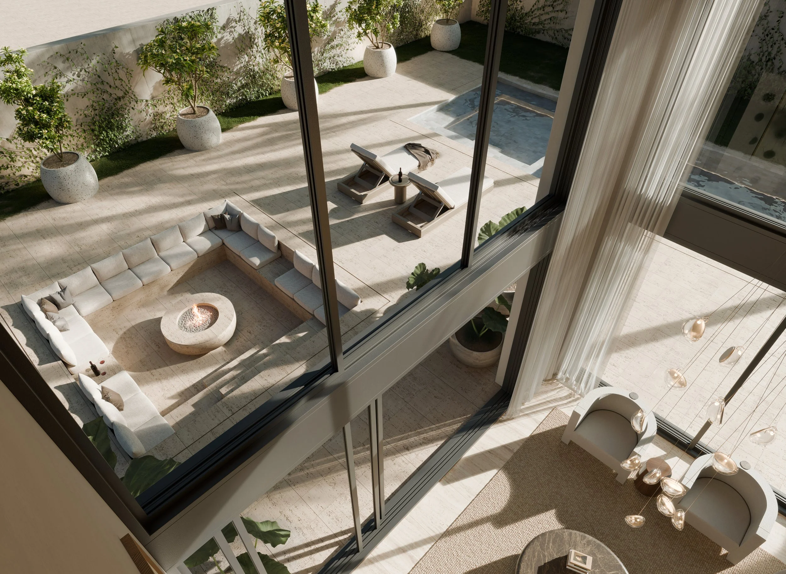 A balcony view showing a covered outdoor seating area with a large U-shaped white sofa and a round firepit, two lounge chairs near a small pool, potted plants, and glass doors leading into an indoor space with a modern chandelier and seating area.