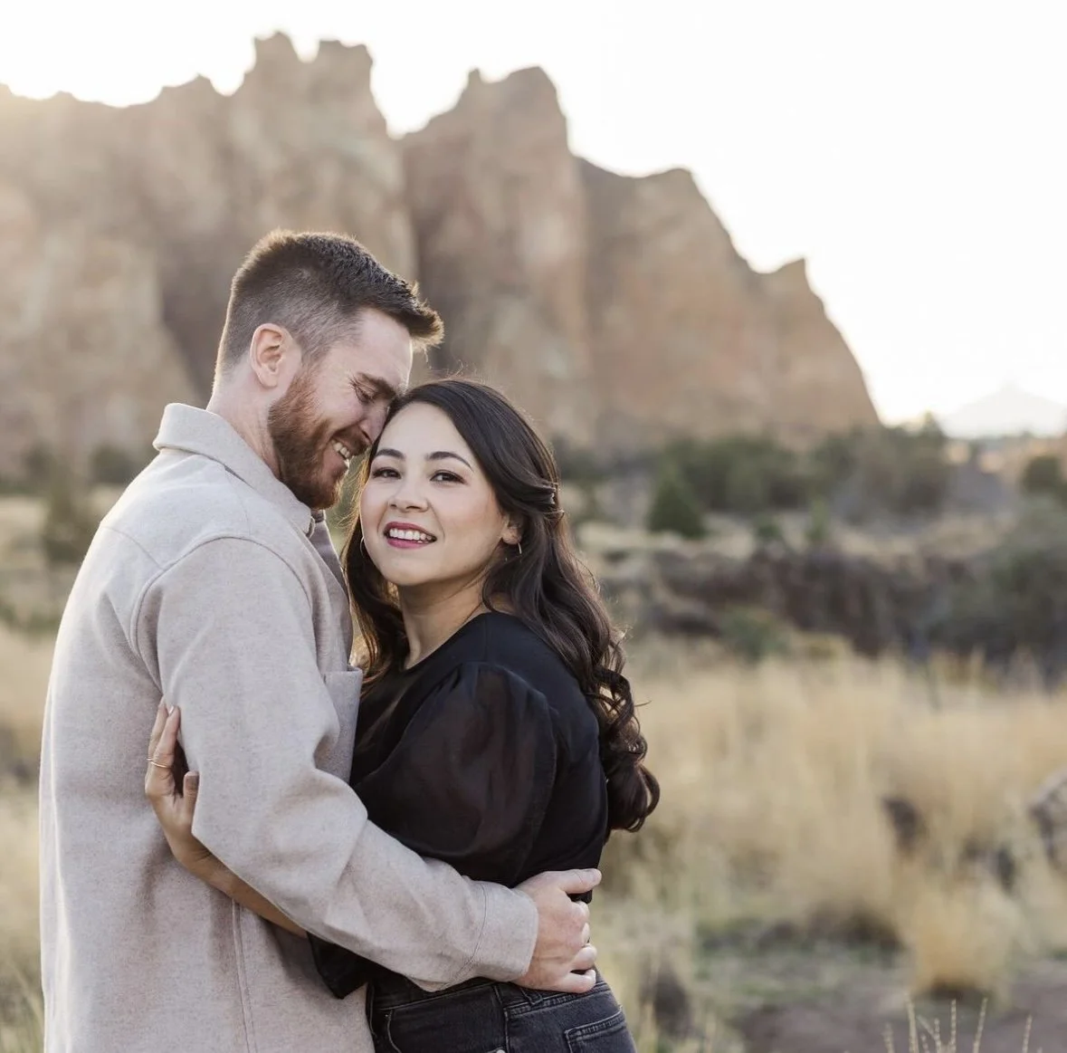 A happy couple embraces outdoors in front of rocky formations with a clear sky.
