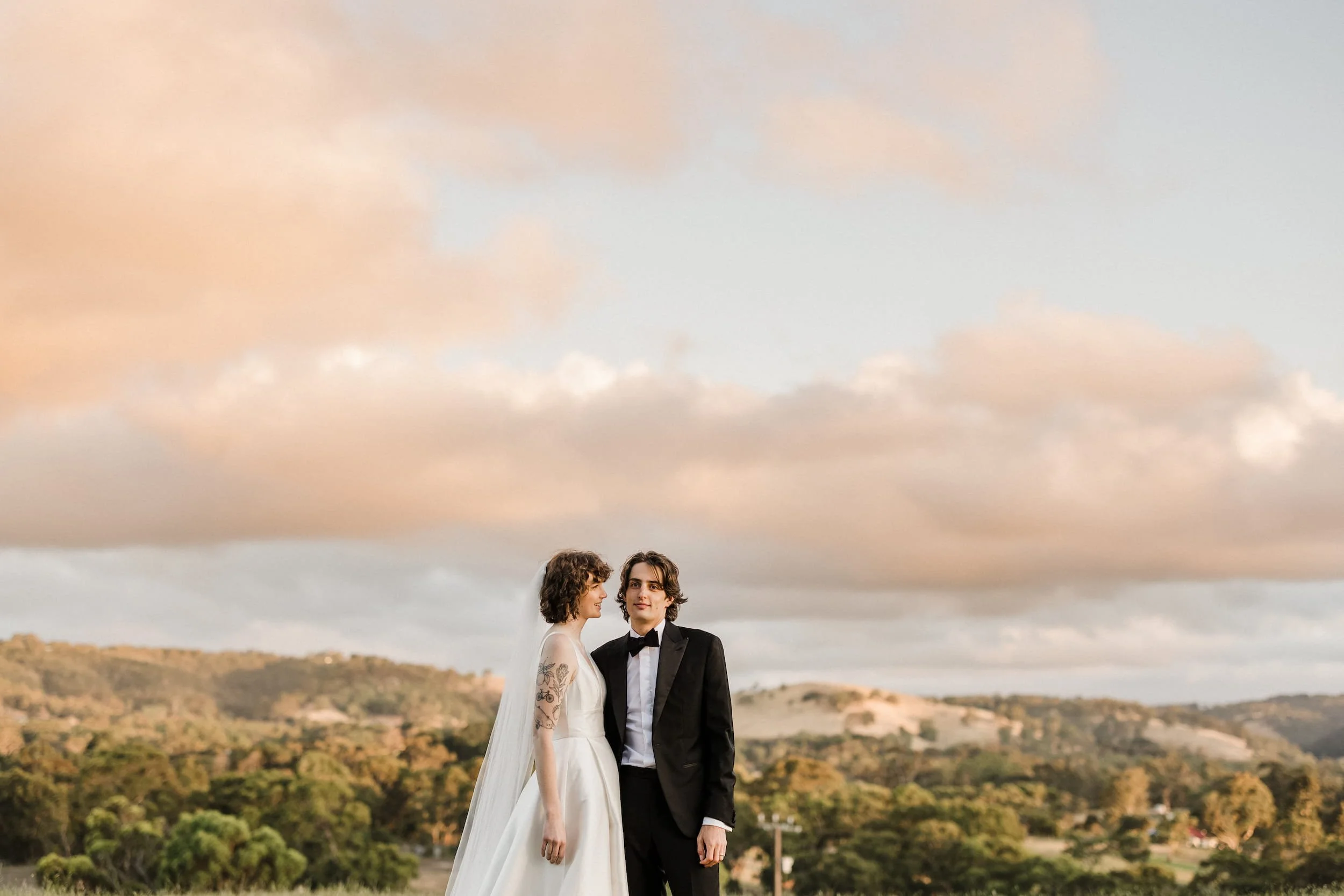 An artistic wedding photograph of an Adelaide couple standing beneath clouds coloured pink during a sunset