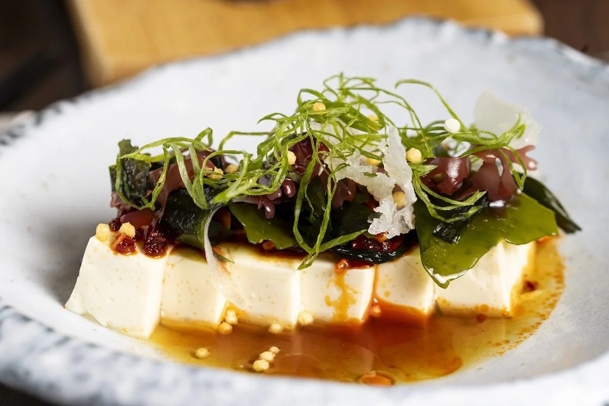 Tofu topped with seaweed, sliced green onion, and bonito flakes in a soy-based sauce.