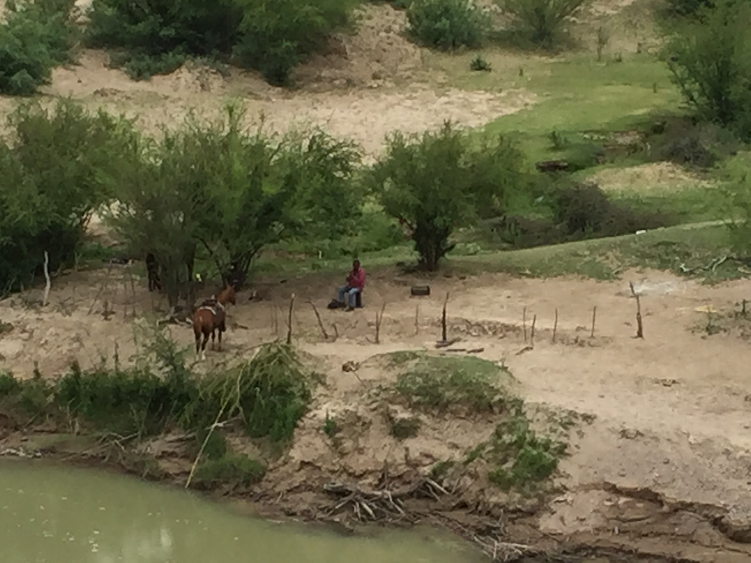 On the Mexican side of the Rio Grande a horseman watches his small group of horses grazing in his corral. 